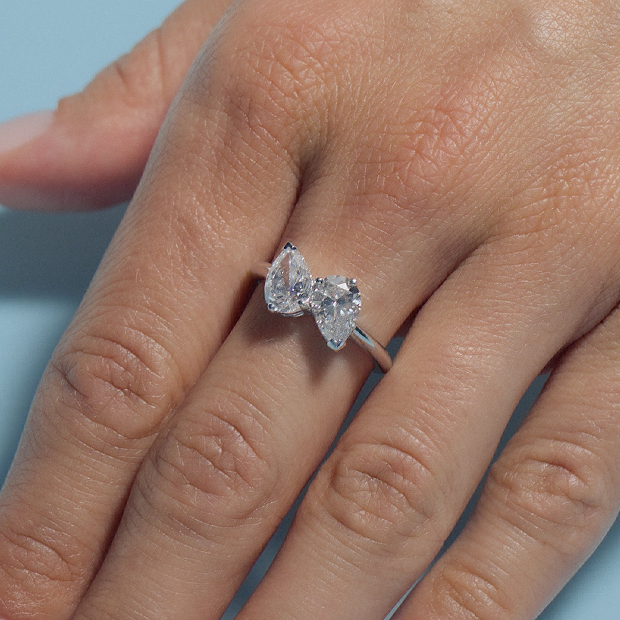 Hand wearing Pear Lab Diamonds Toi & Moi Ring on a light blue background