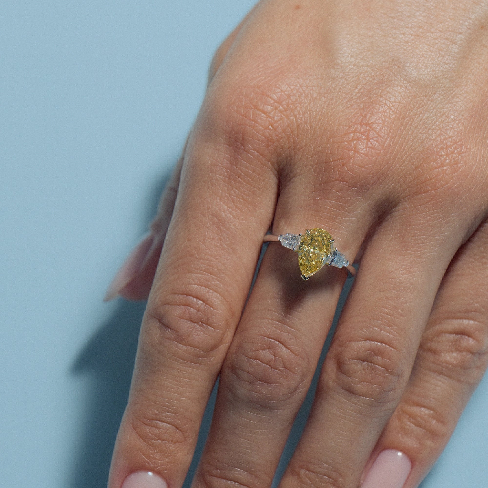 Fancy Intense Yellow Pear Lab Diamond Classic Trilogy ring on a hand against a light blue background