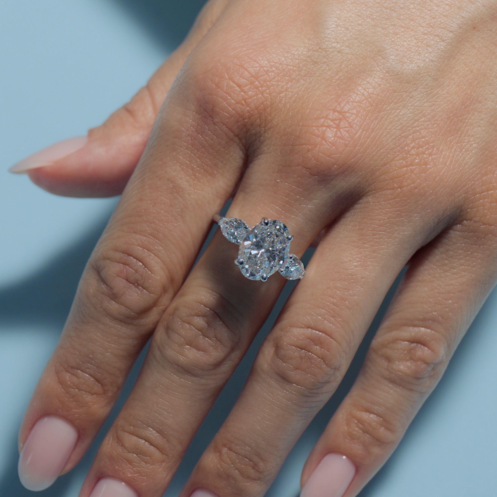 Oval Lab Diamond Pear Trilogy ring on model's hand with a light blue background