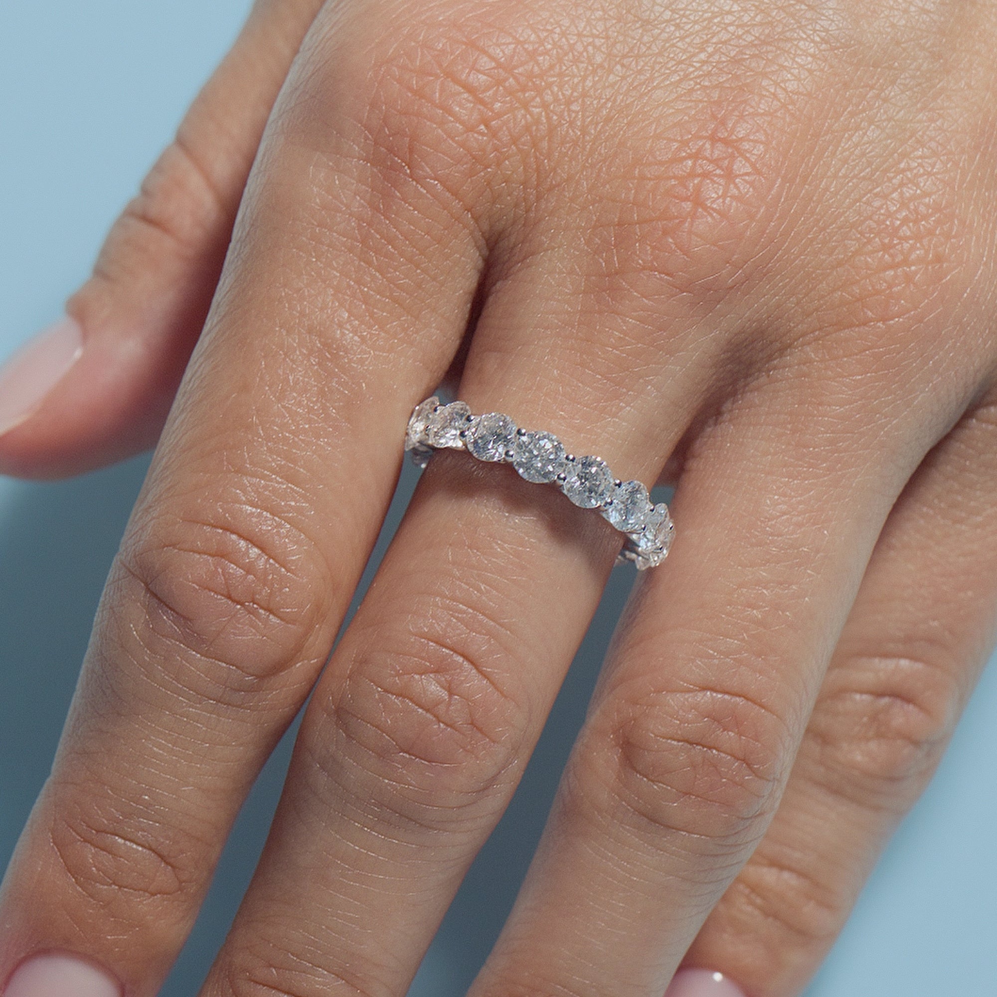Round Lab Diamonds Eternity Ring on a person's finger against a light blue background