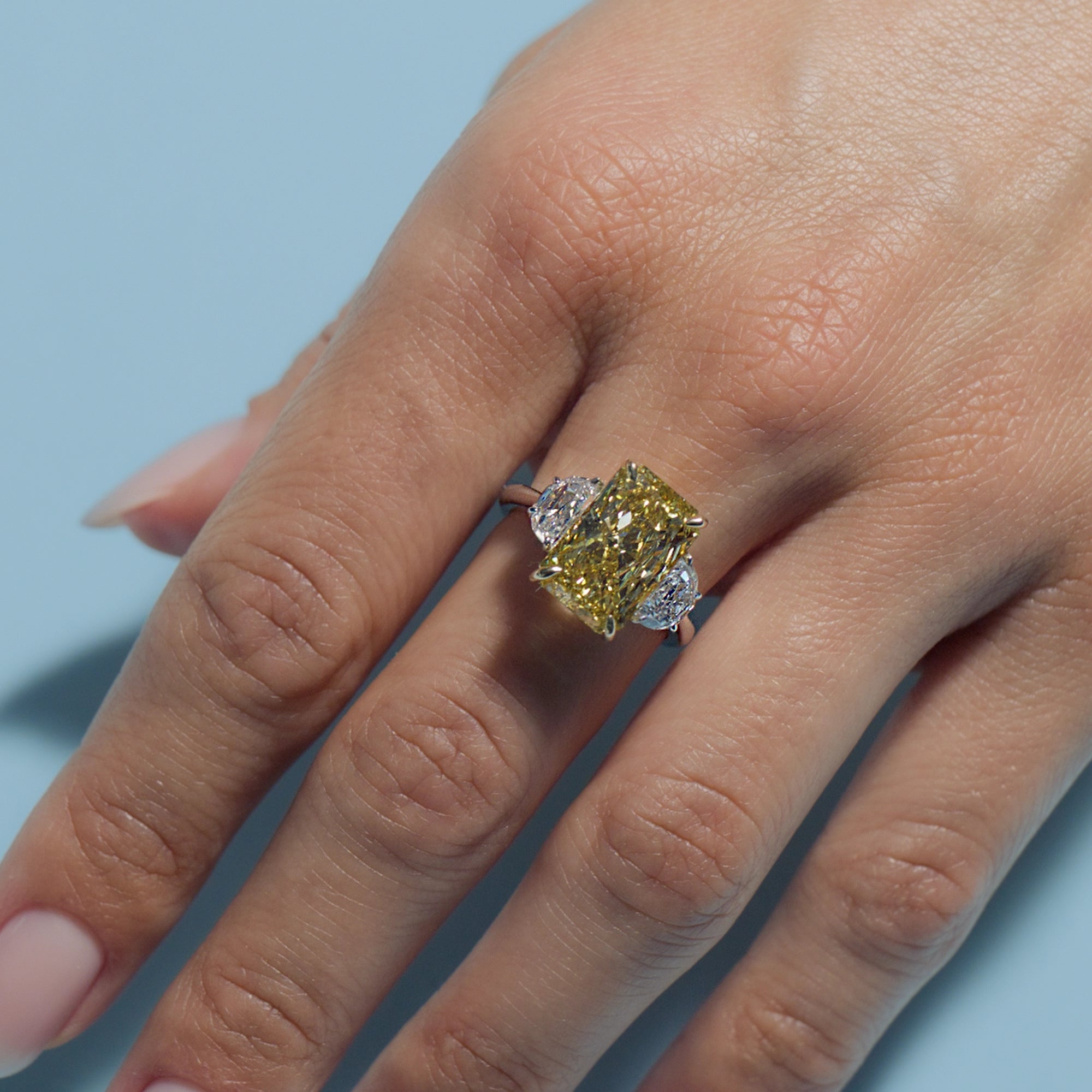 Fancy Intense Yellow Radiant Lab Diamond Classic Trilogy ring on a hand against a light blue background