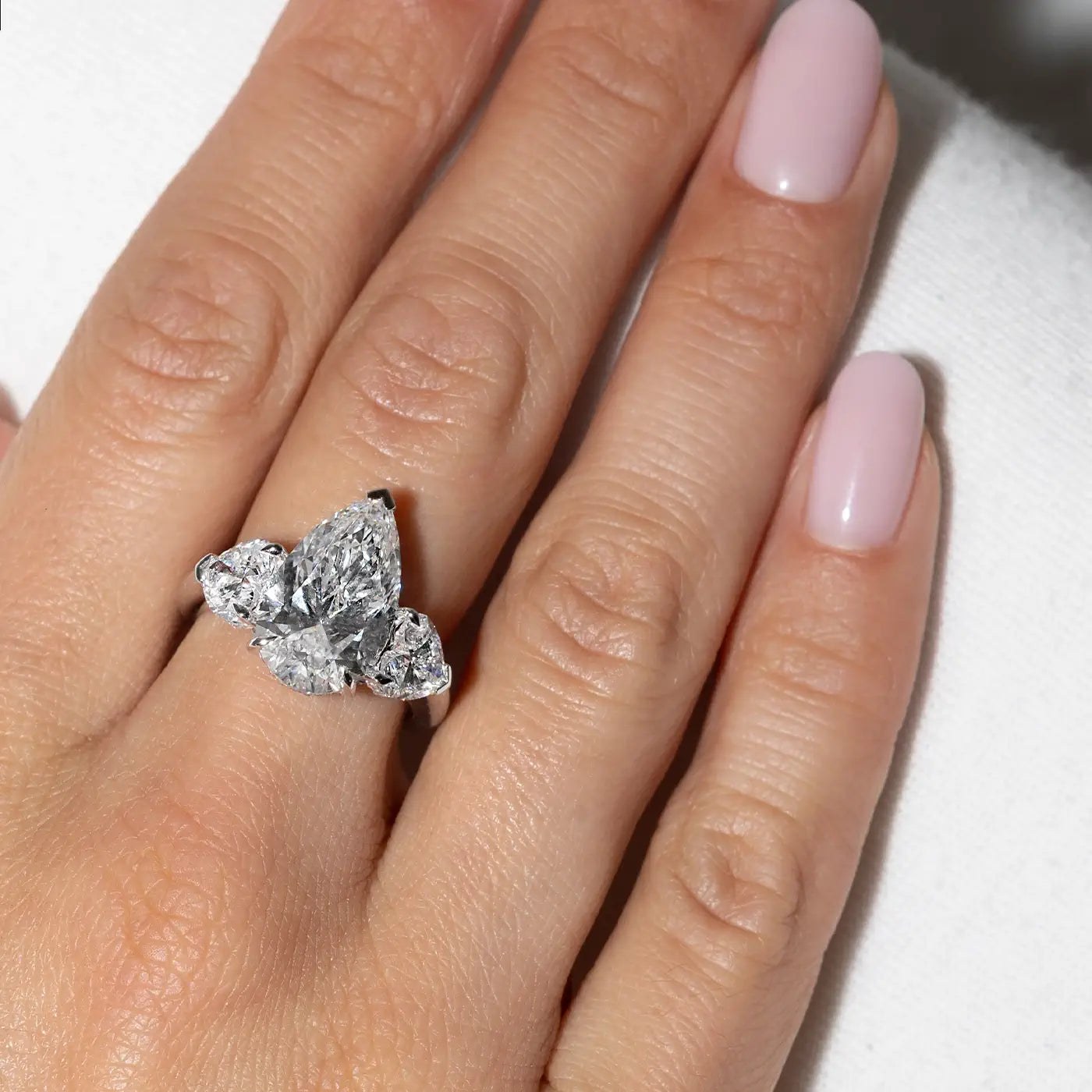 A pear-cut lab diamond ring with heart side stones worn on hand by the model