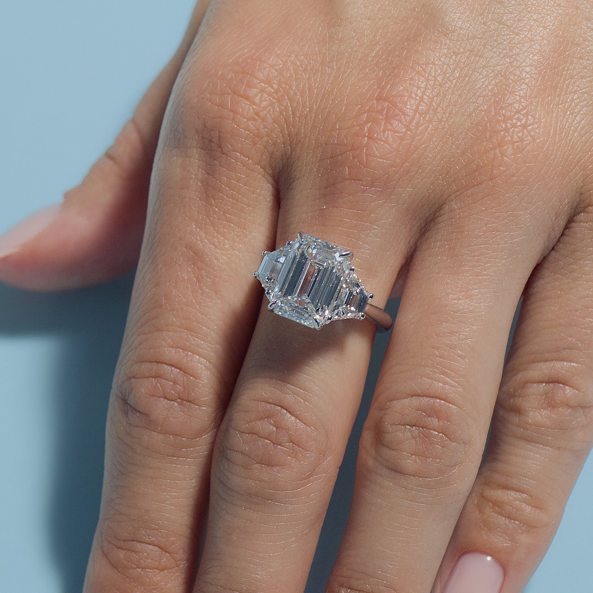 Emerald Lab Diamond Classic Trilogy Ring on a finger against a light blue background