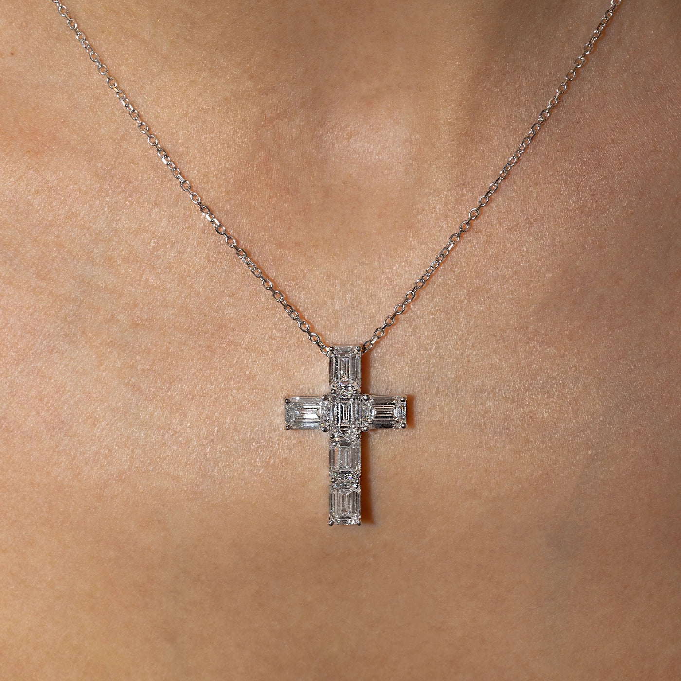 Emerald-cut lab-grown diamond cross pendant necklace in white gold, worn on the neck.