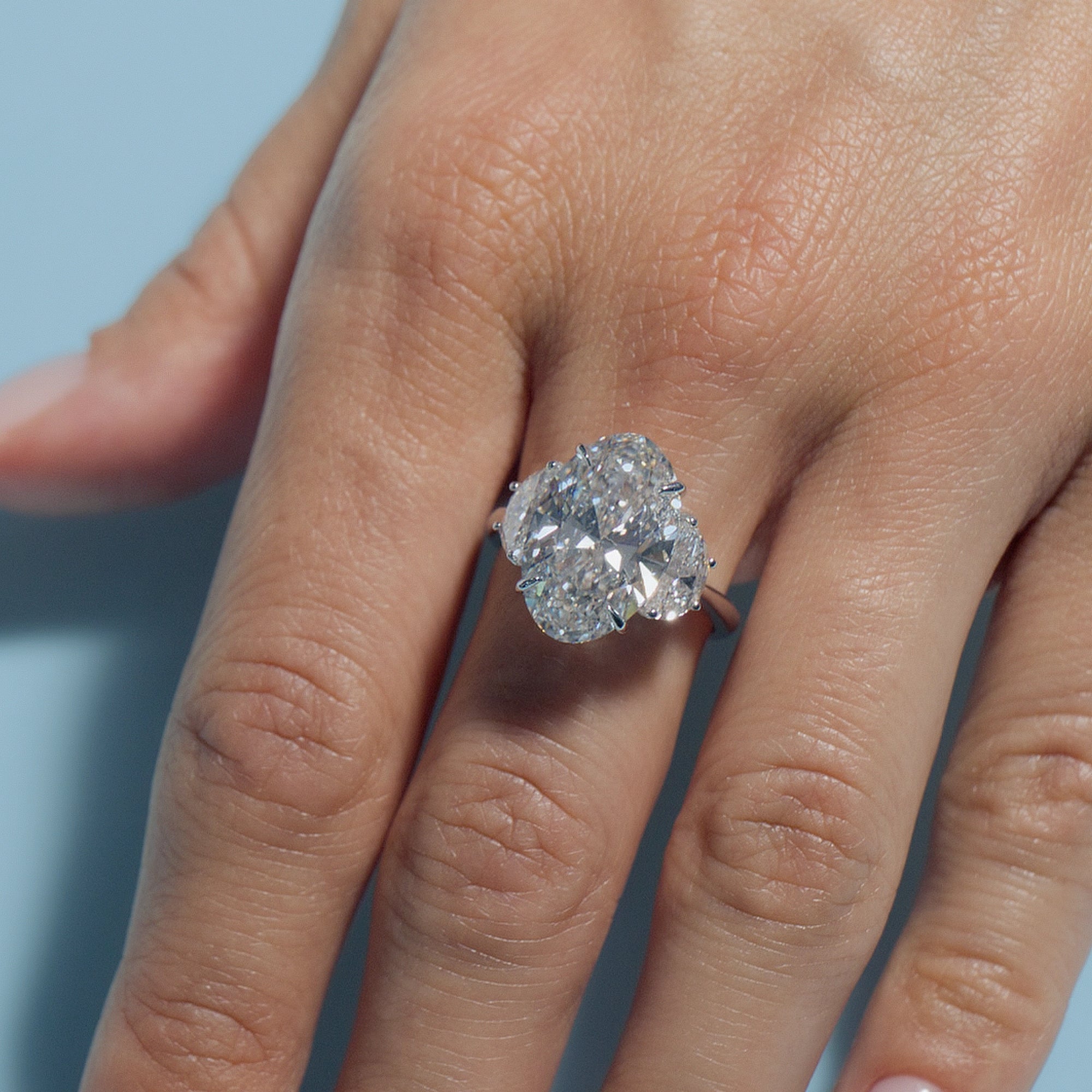 6.5ct Oval Lab Diamond Classic Trilogy ring on a model's finger against a light blue background