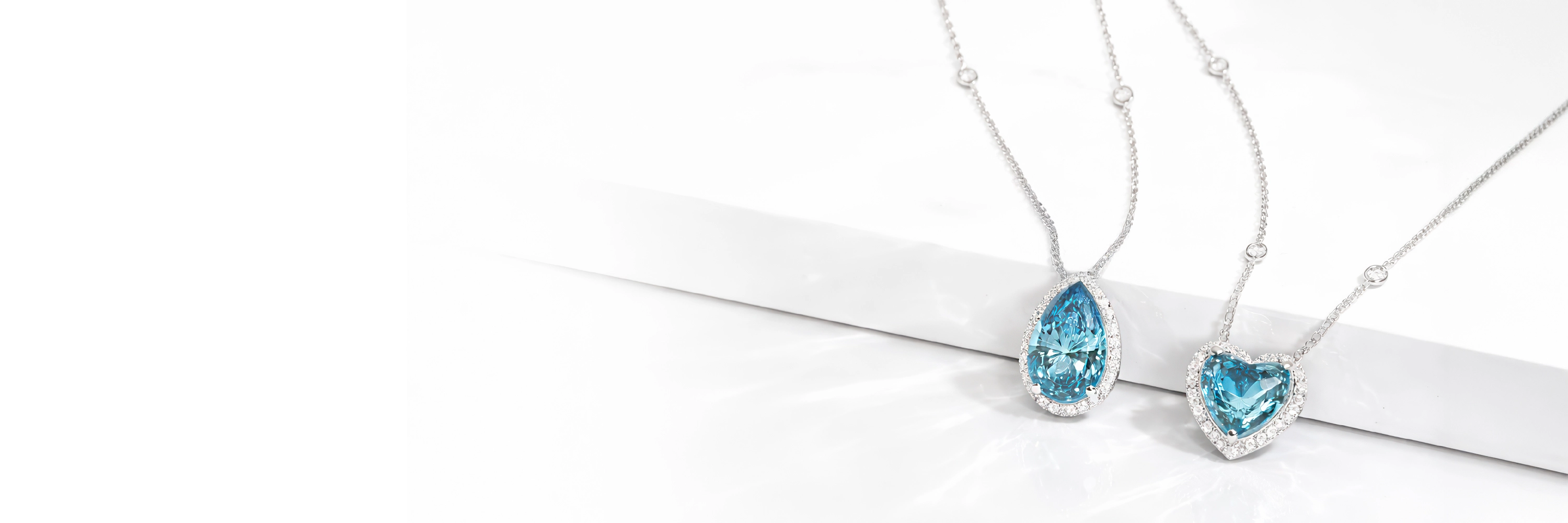 Two lab grown diamond halo necklaces featuring pear and heart-shaped blue gemstones on white background
