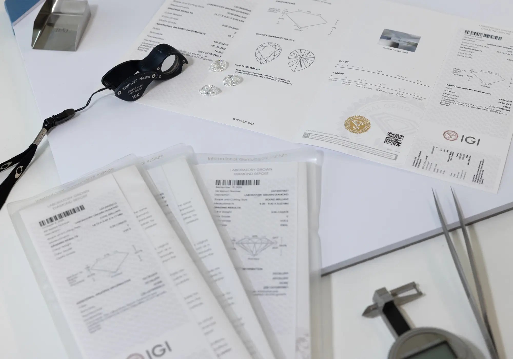 Diamond grading reports, loose lab-grown diamonds, and gem tools are spread out on a white desk.