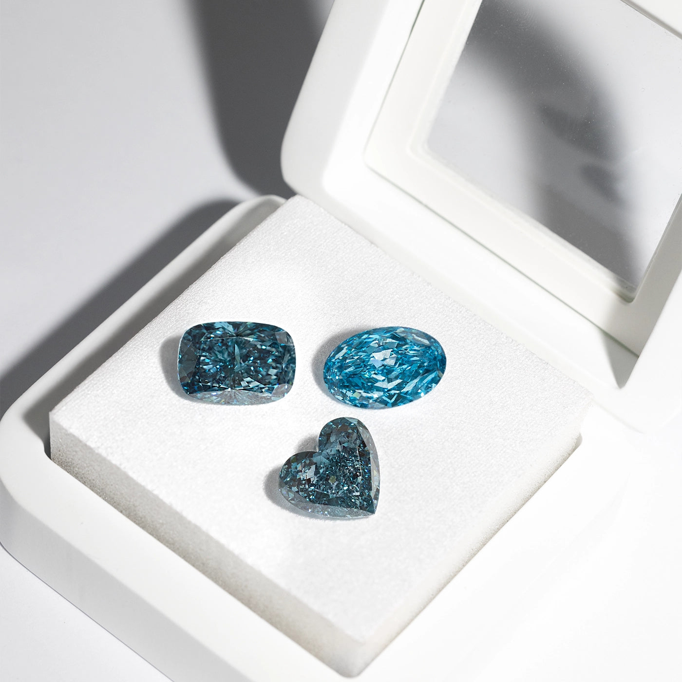 Fancy blue loose lab diamonds in cushion, oval, and heart cuts with vivid color displayed in a luxury white jewelry box