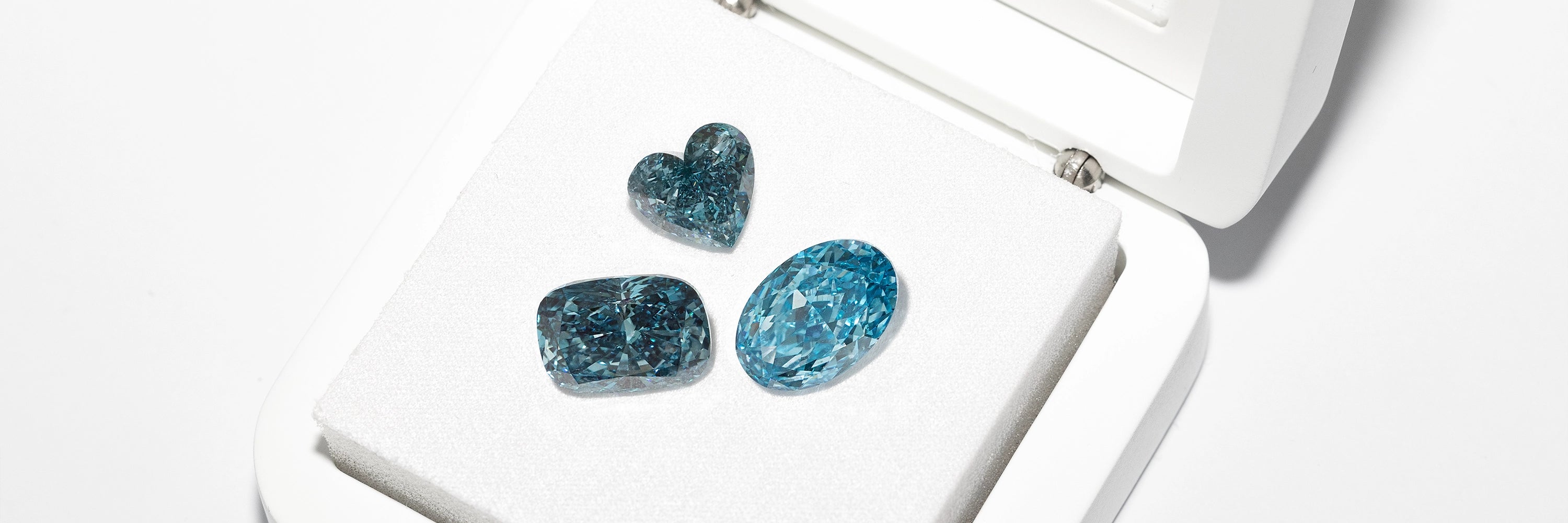 Fancy blue loose lab diamonds in heart, cushion, and oval cuts displayed in jewelry box by BÄL Diamonds