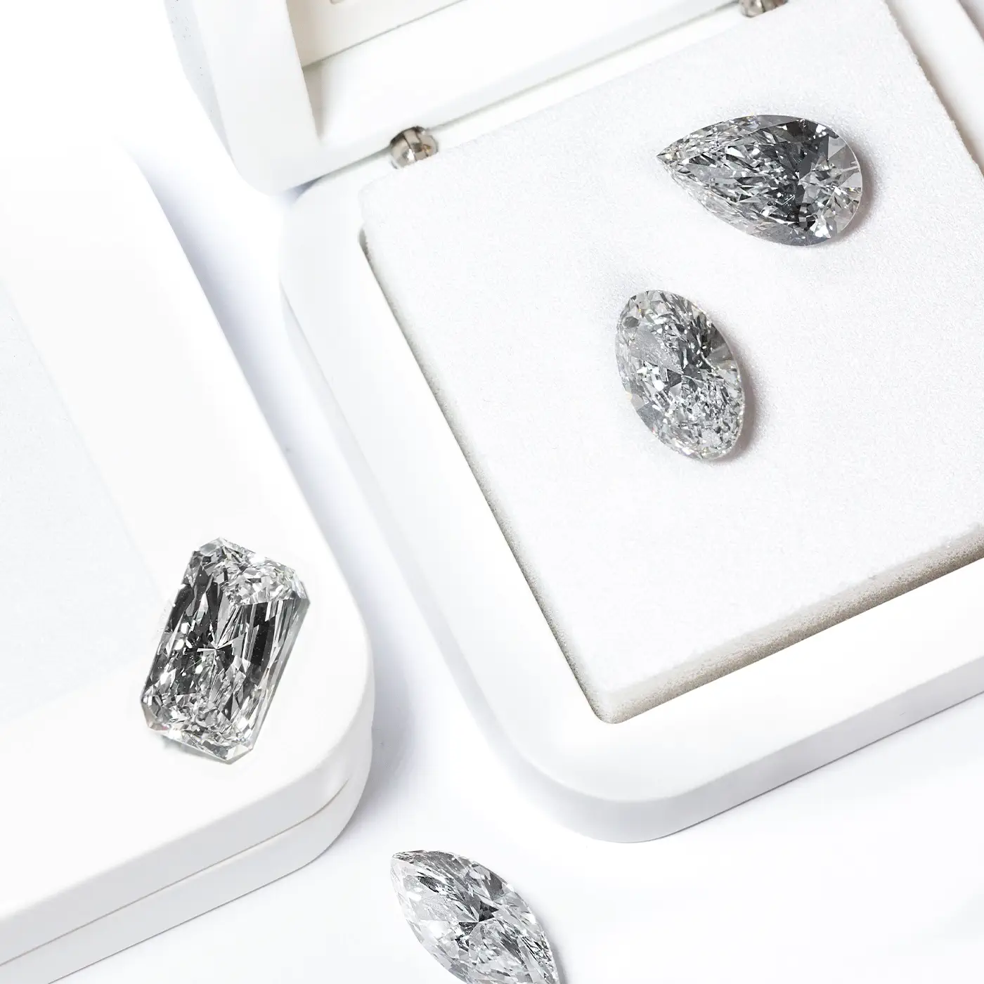 White loose lab diamonds in radiant, oval, marquise and pear cuts displayed in luxury white jewelry boxes by BÄL Diamonds