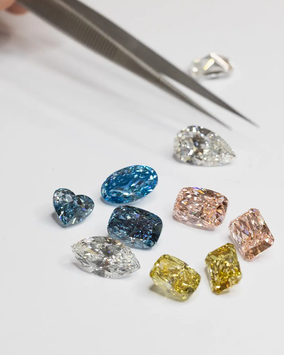 Bal Loose Fancy Colored Diamonds in different shapes and a tweezer as a tool for holding loose diamonds