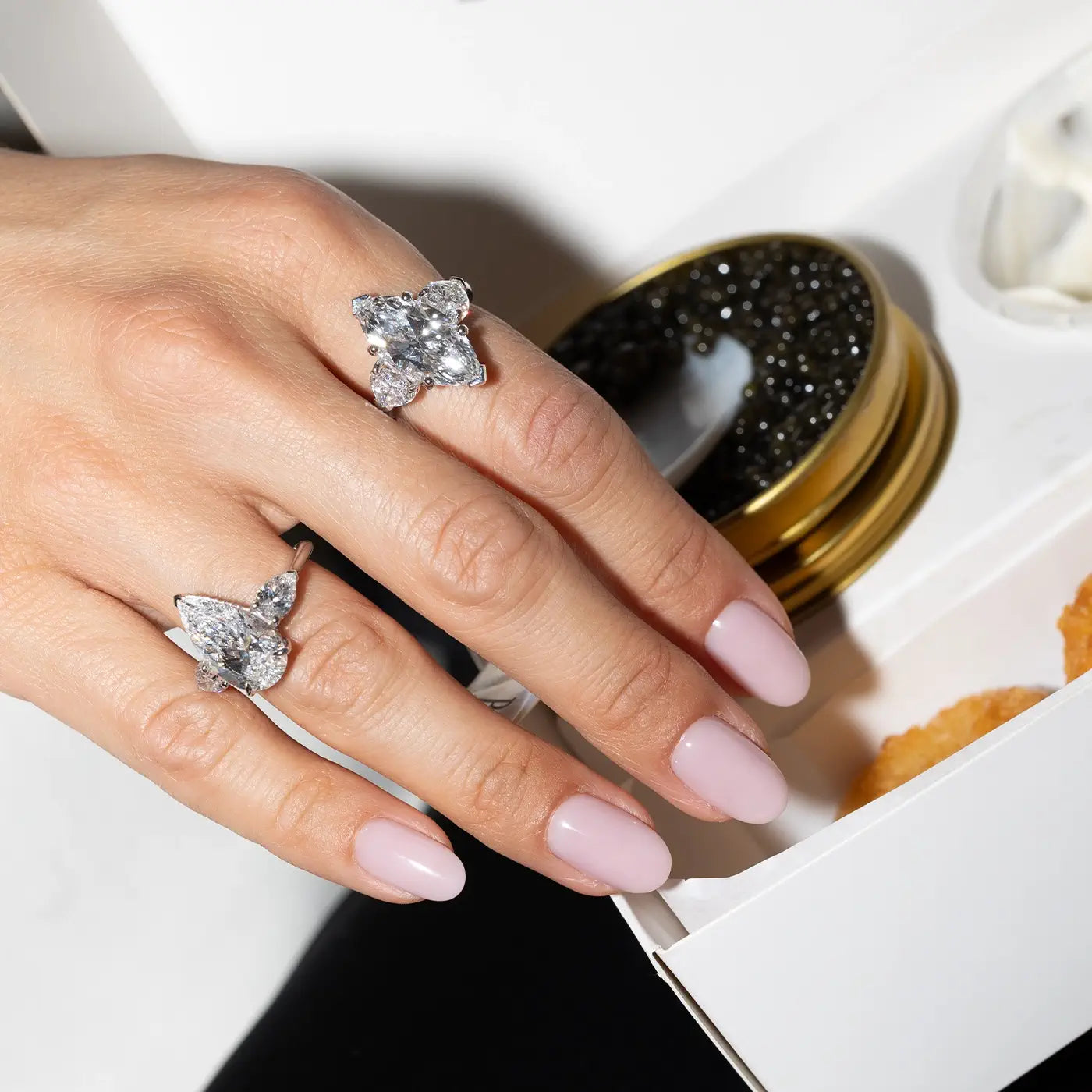 A model's hand wearing 2 different shaped diamond ring from Bal while grabbing some caviar.