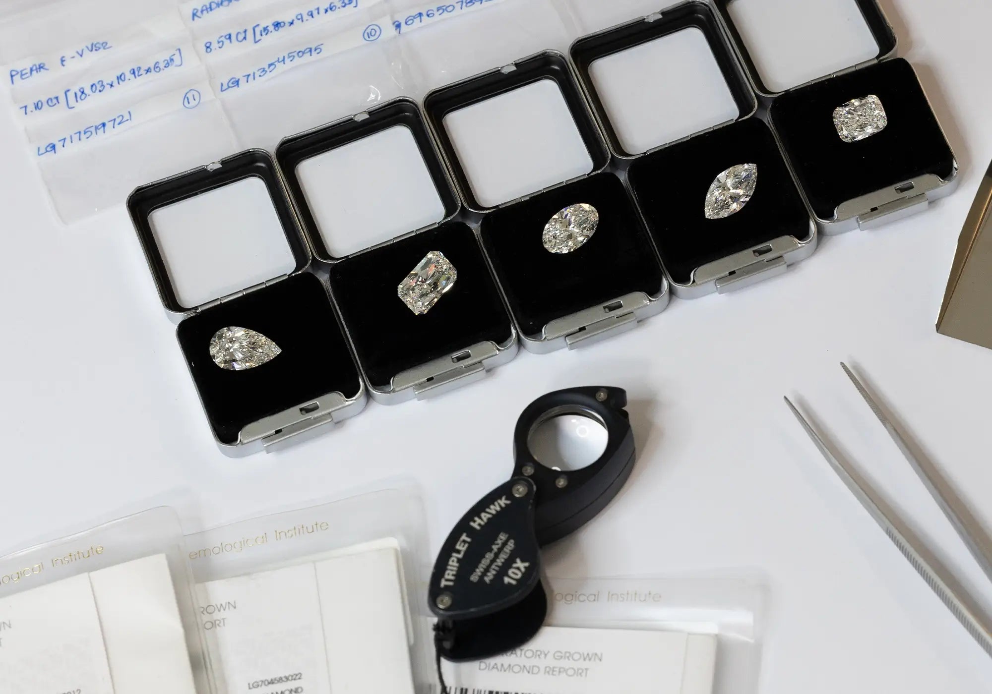 Different cuts of diamonds on top of each case surrounded by tools, pouches and certificates