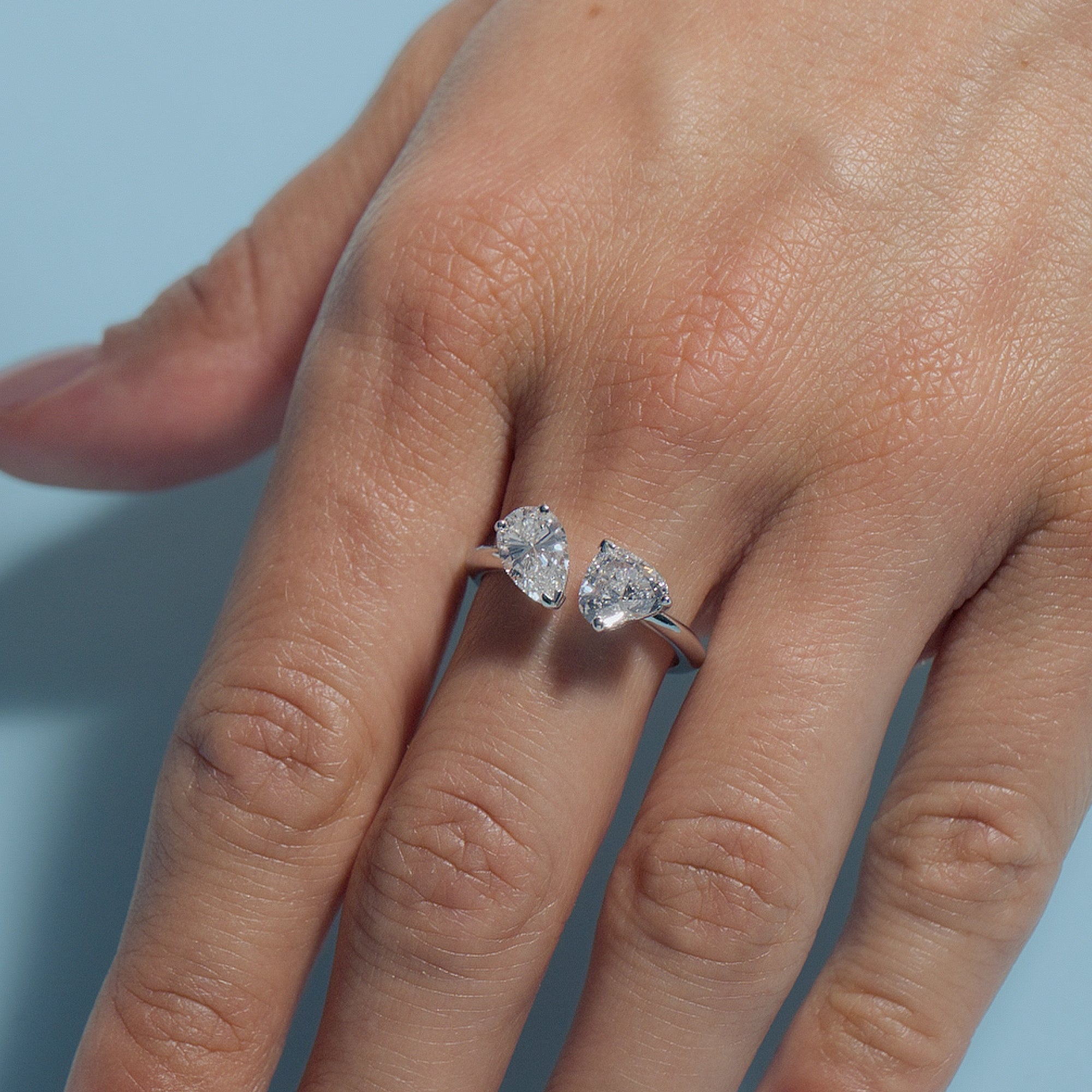 Hand wearing a Pear-Heart Lab Diamonds Toi & Moi Ring against a light blue background