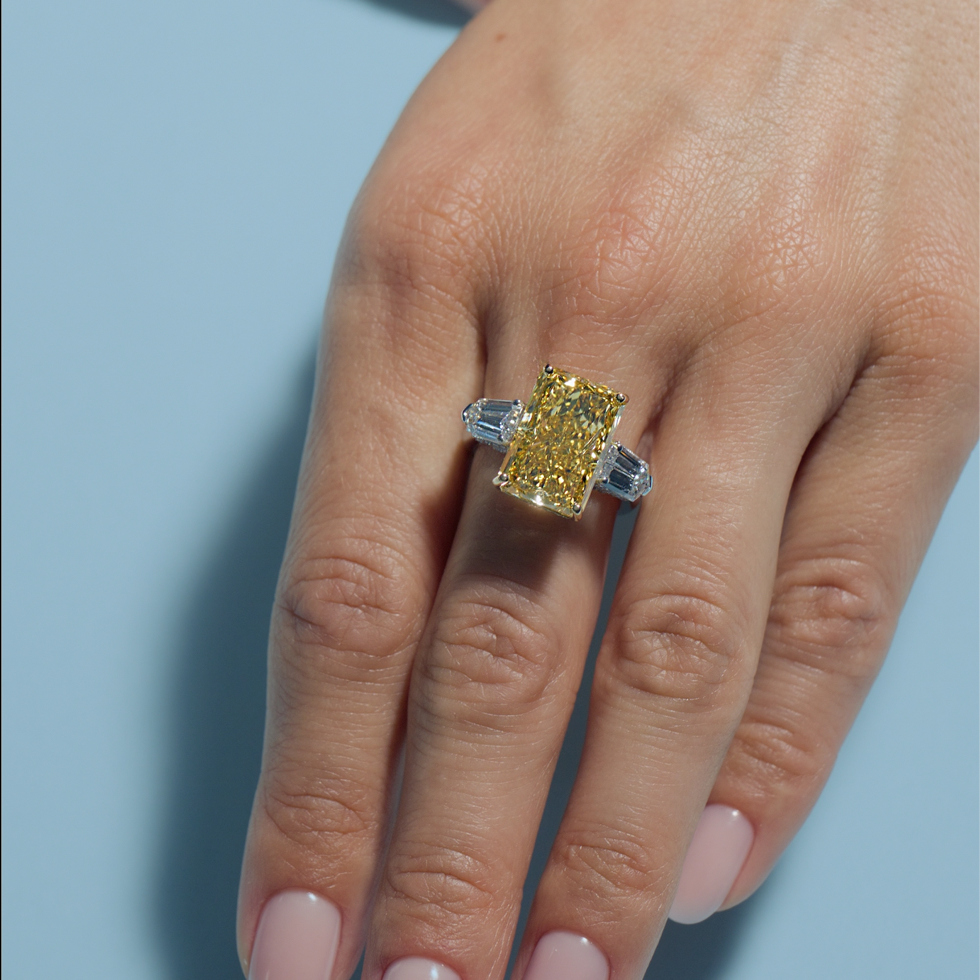 Fancy Vivid Yellow Radiant Lab Diamond Intricate Trilogy Ring on a hand against a light blue background