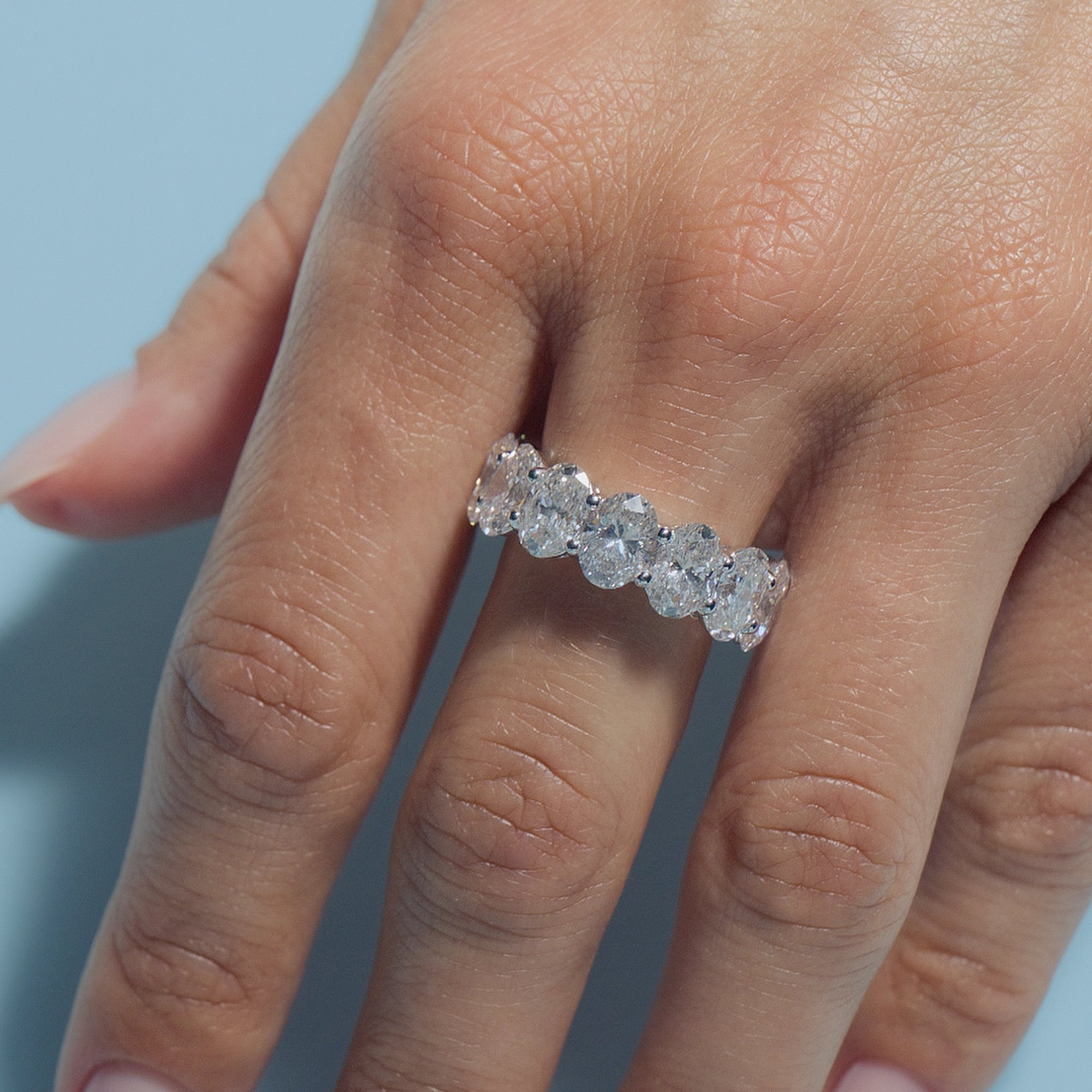 Oval Lab Diamonds Eternity Ring on a model's finger against a light blue background