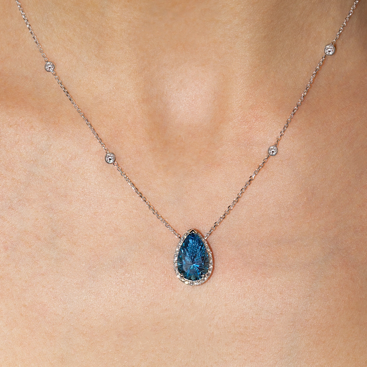 Pear-shaped blue lab-grown diamond halo pendant necklace in white gold with sautoir, worn on the neck.