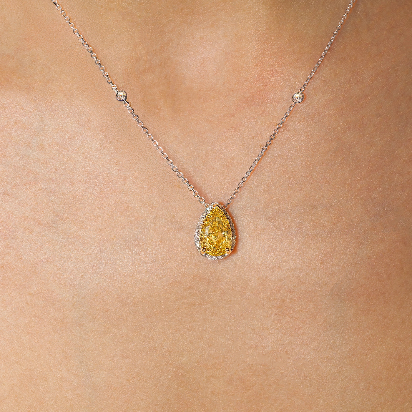 Pear-shaped yellow lab-grown diamond halo pendant necklace in white gold with sautoir, worn on the neck.