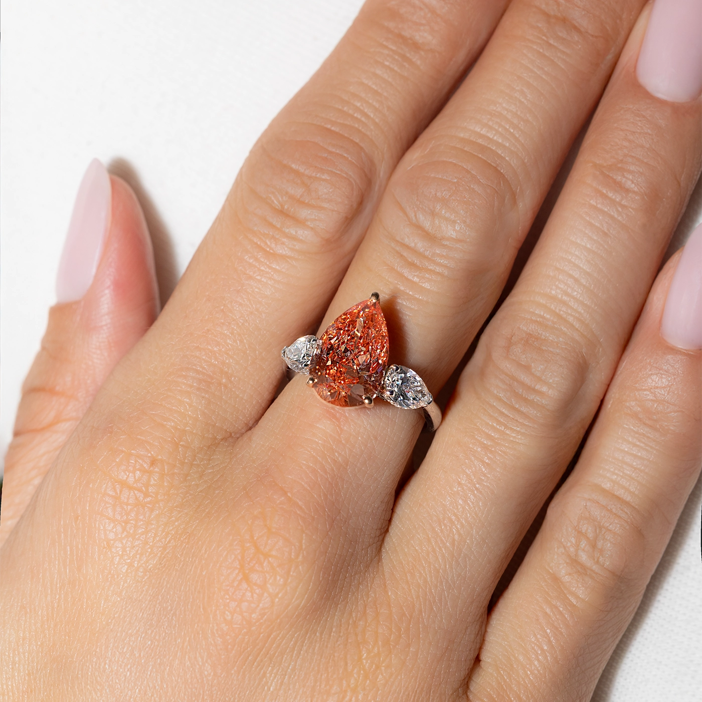 Fancy Vivid Orangy Pink Lab Diamond with pear side stones worn on the hand of the model