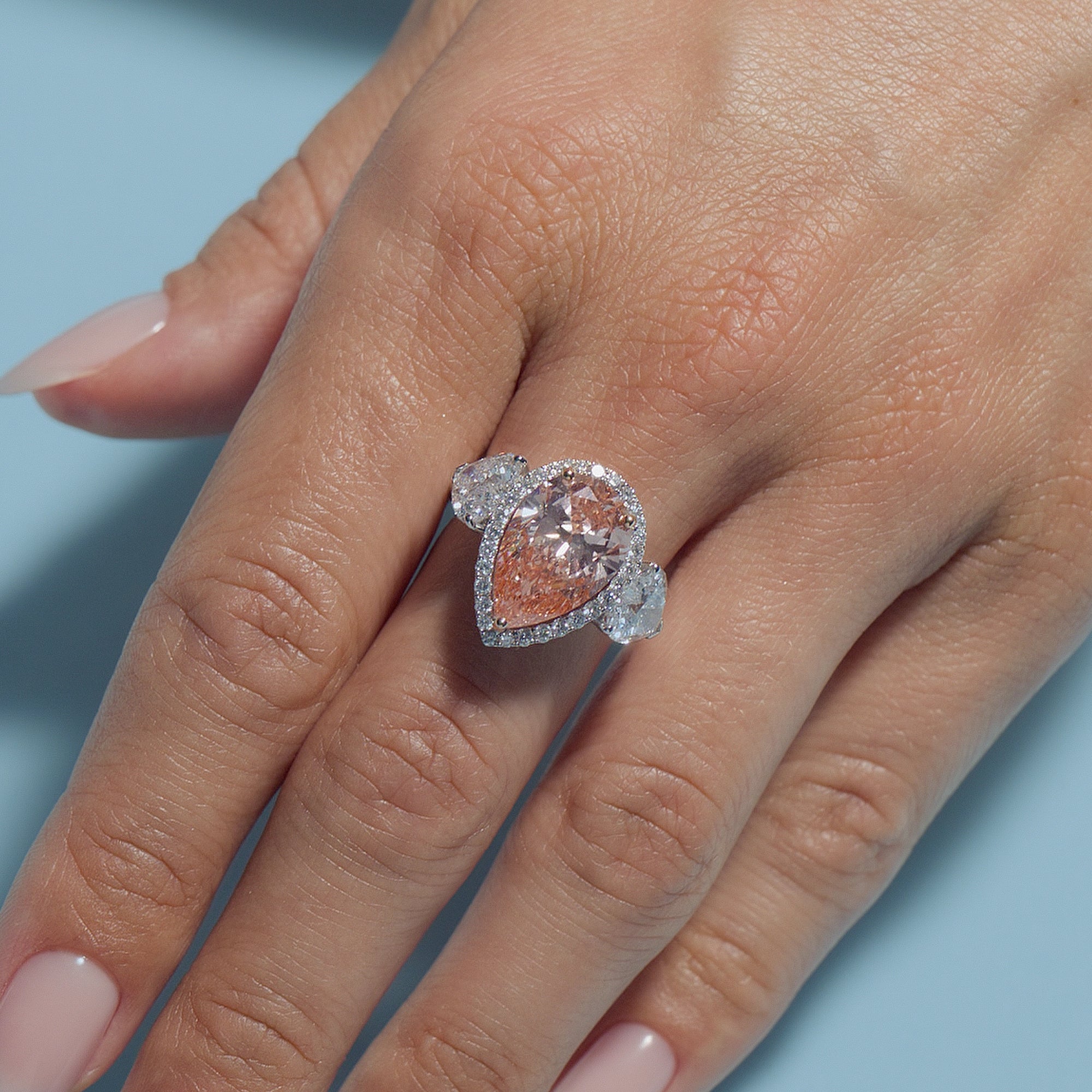 Pear Fancy Vivid Pink Lab Diamond Heart Trilogy ring on a hand with a light blue background