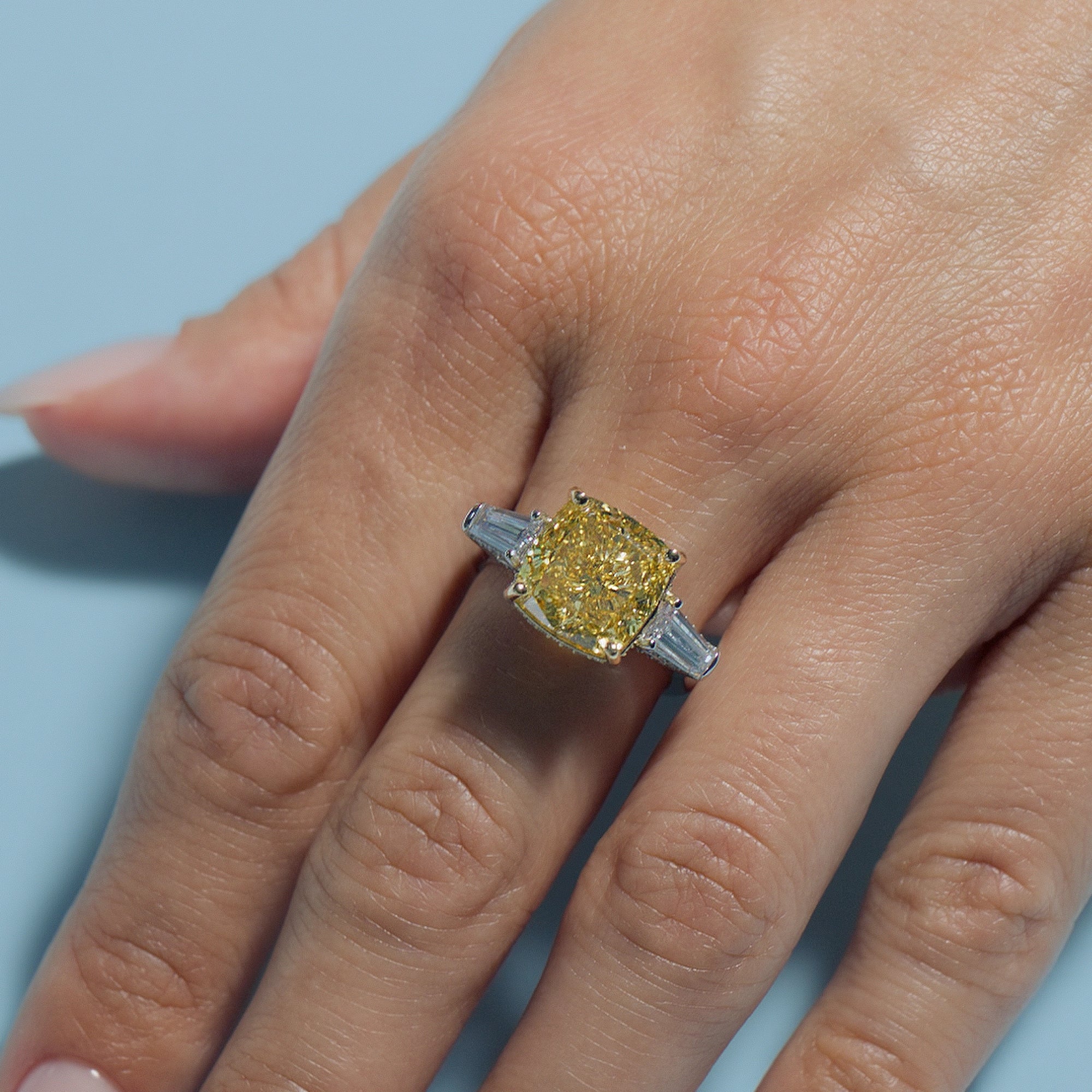 6.7ct Fancy Vivid Yellow Square Cushion Lab Diamond Intricate Trilogy ring on a hand with a light blue background