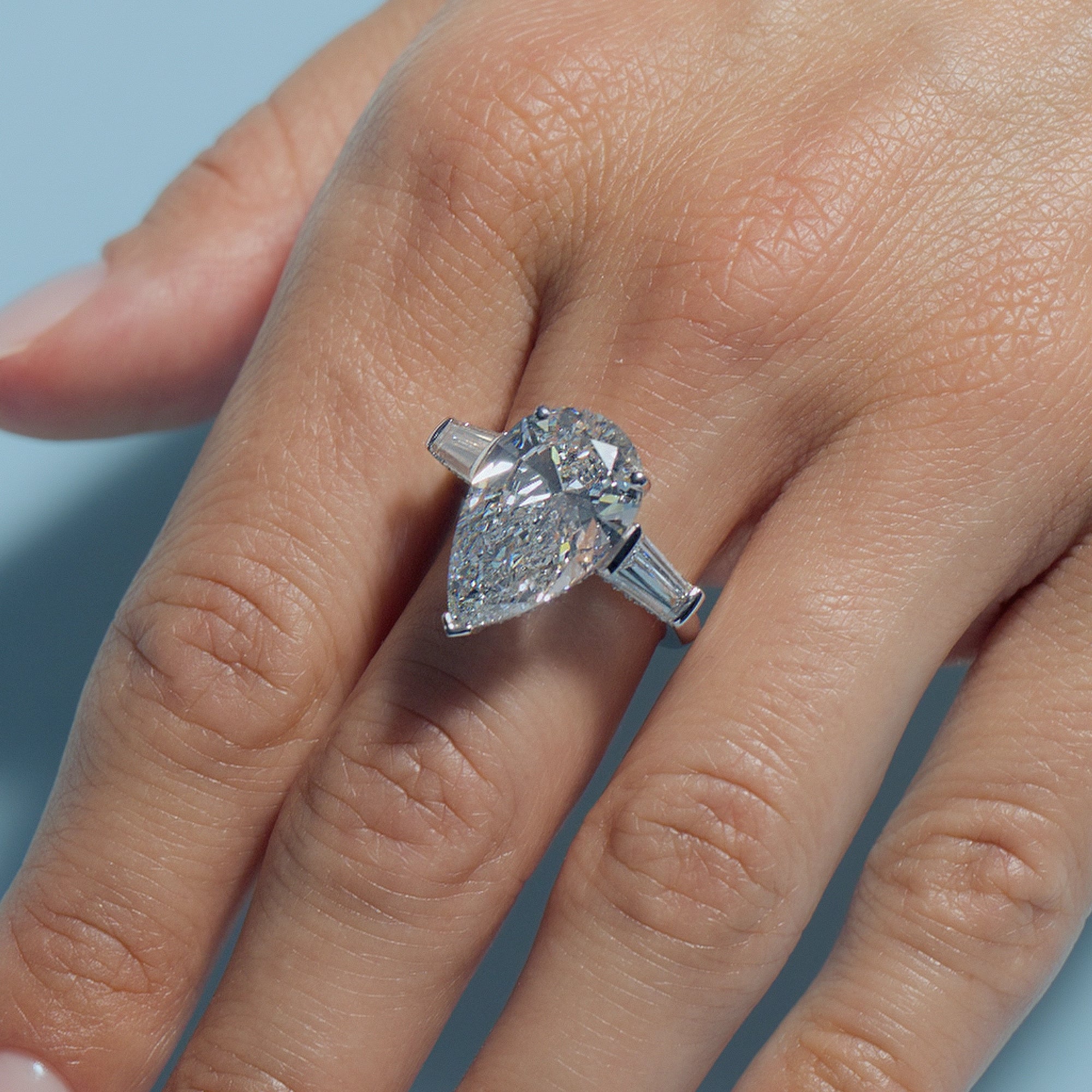 7.1ct Pear Lab Diamond Intricate Trilogy ring on a model's finger against a light blue background