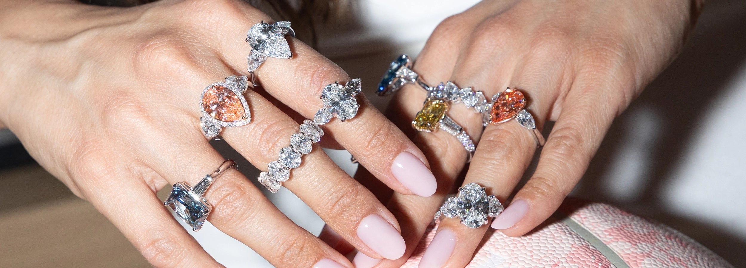 Close-up of two hands wearing multiple lab diamond rings, featuring a mix of white and fancy-colored diamonds on top of a pink basketball 