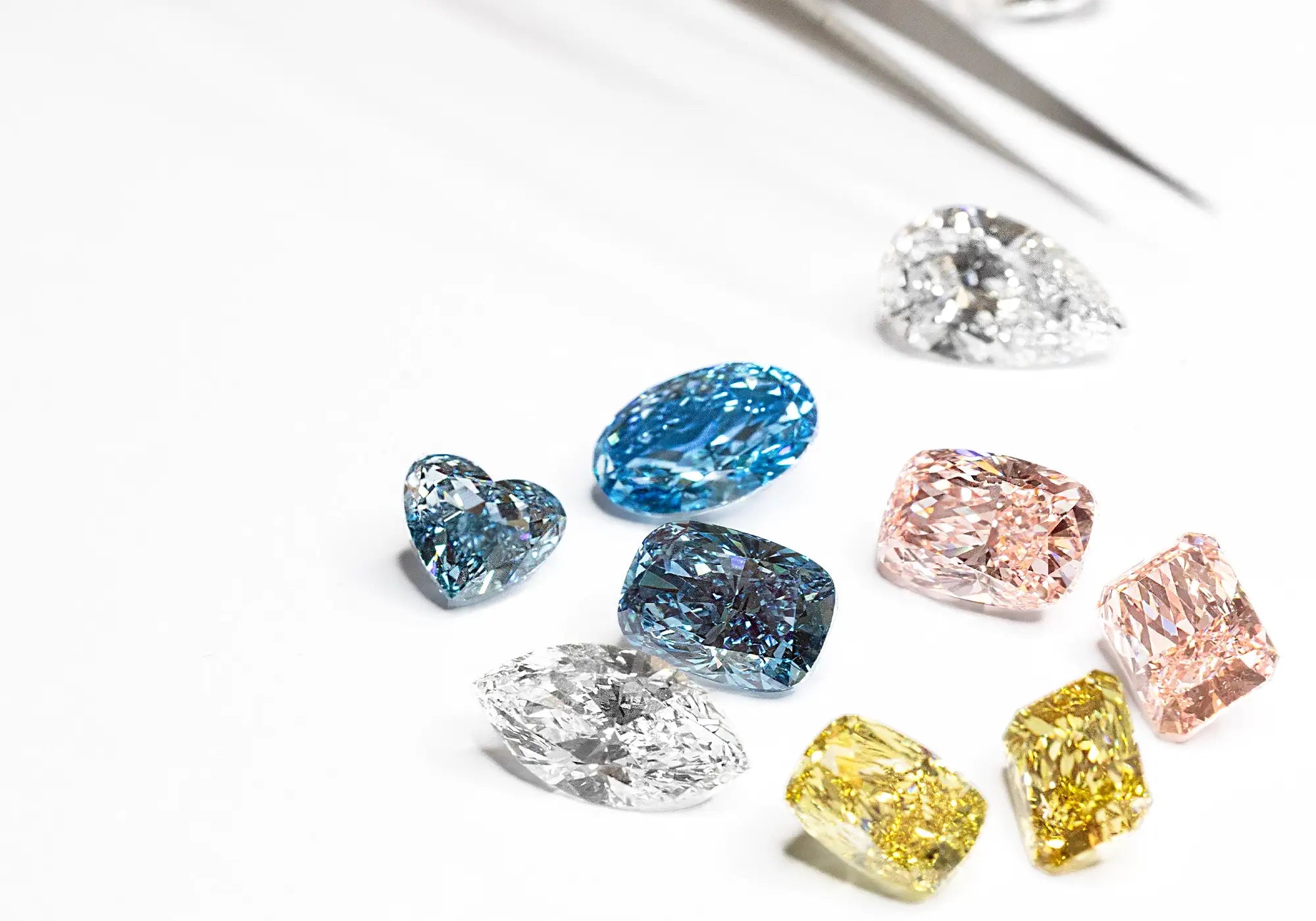 Scattered Fancy Colored and White Loose Lab Grown Diamonds on a white surface with tweezer
