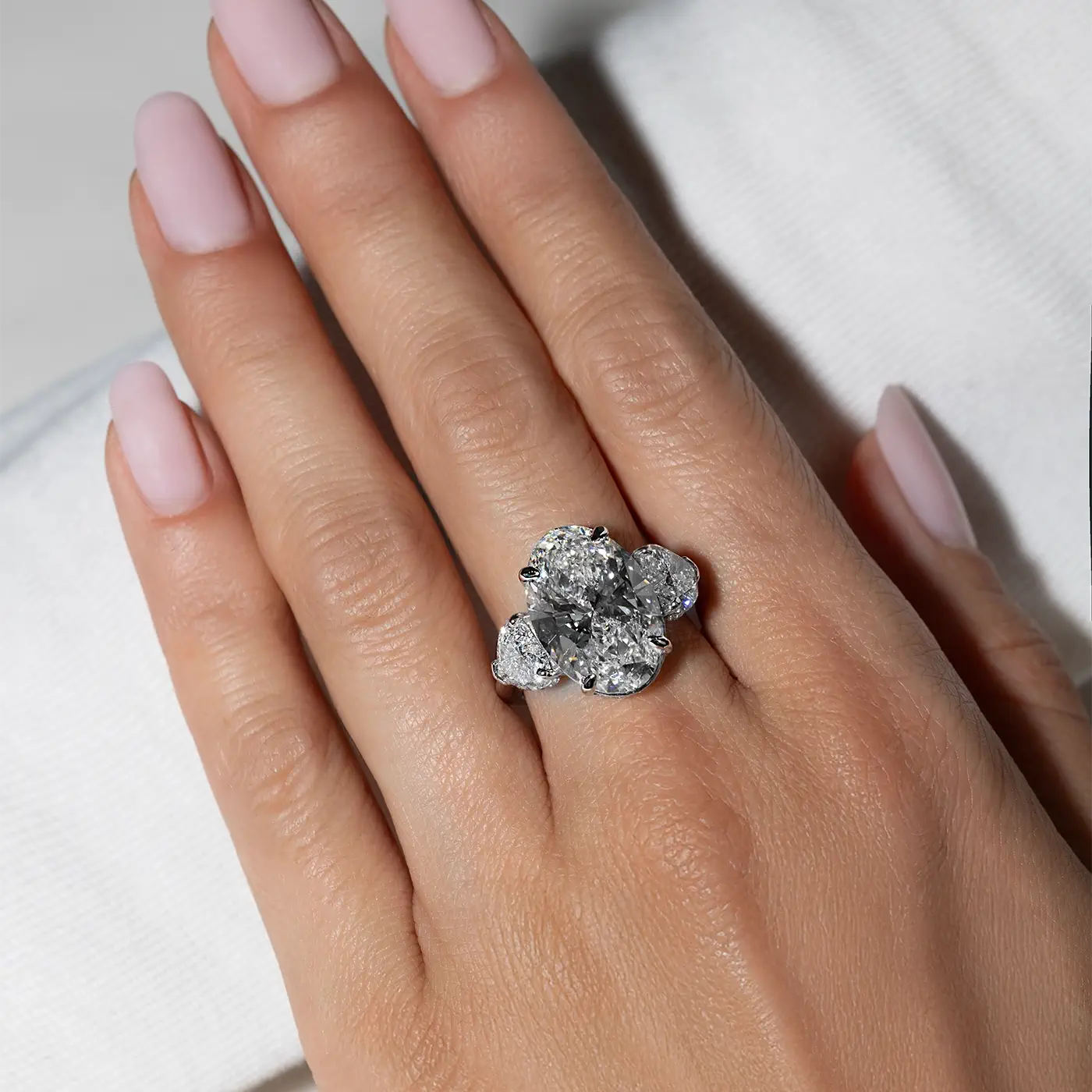 An oval-shaped lab diamond with heart side stones in 18k white go worn on hand by the model