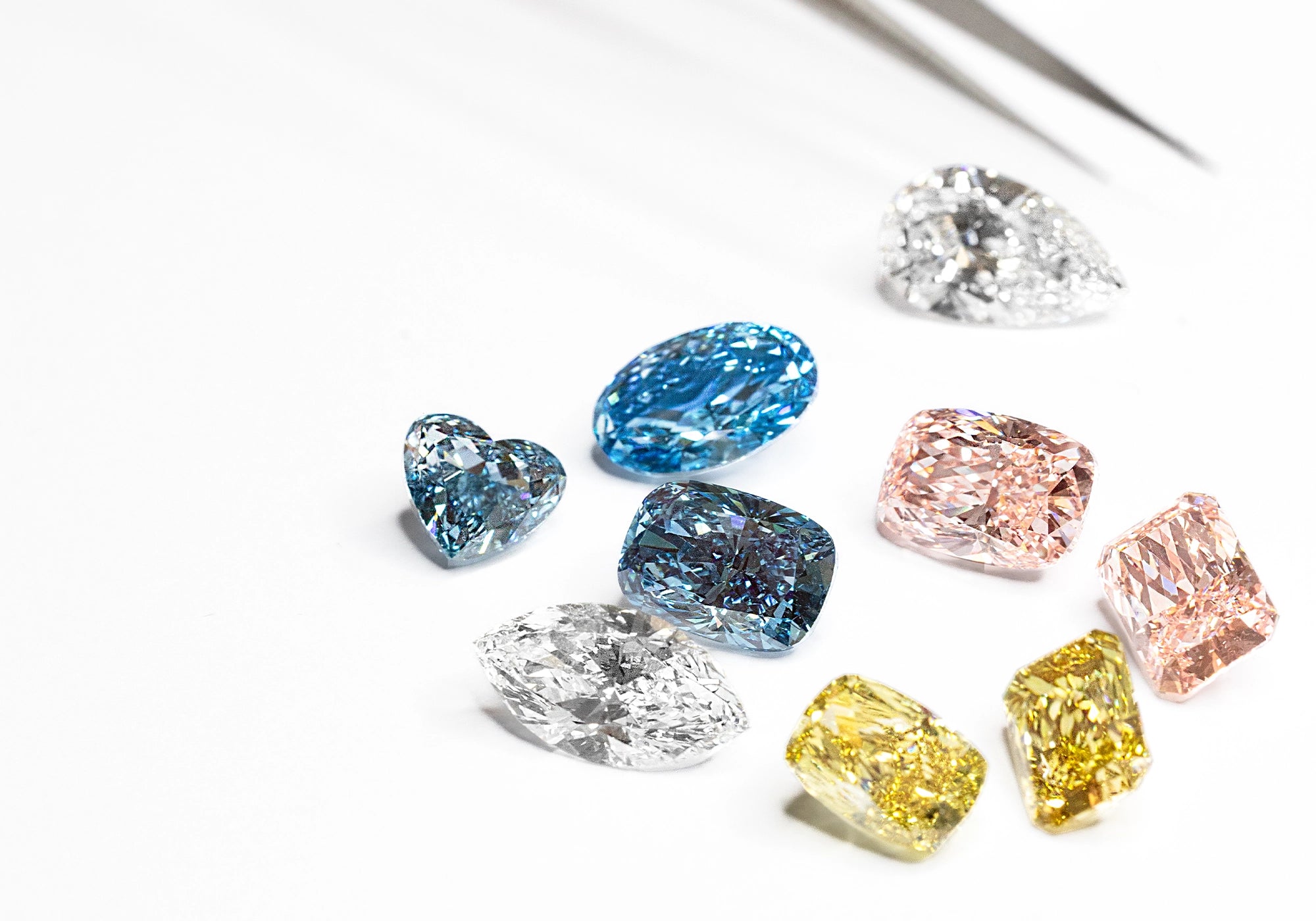 Fancy-cut colored loose diamonds including oval, cushion, pear, and heart shapes arranged on a white background