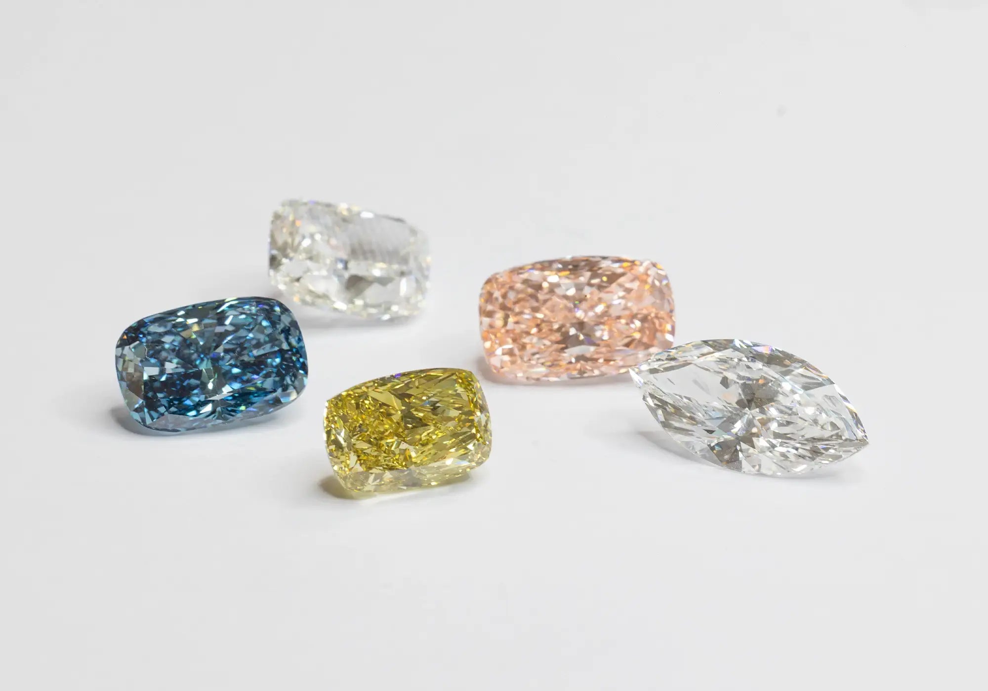 Five fancy colorful, faceted lab-grown diamonds are arranged on a clean white background.