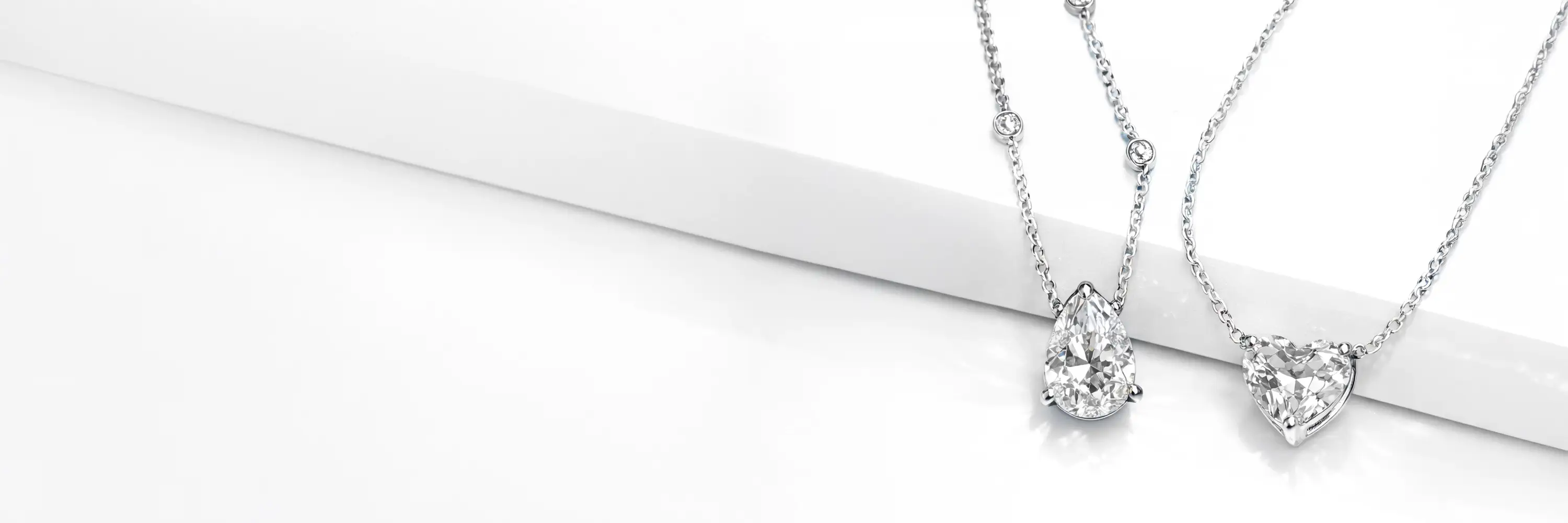 Pear-cut and heart-cut white lab diamond pendant necklaces displayed on a white surface