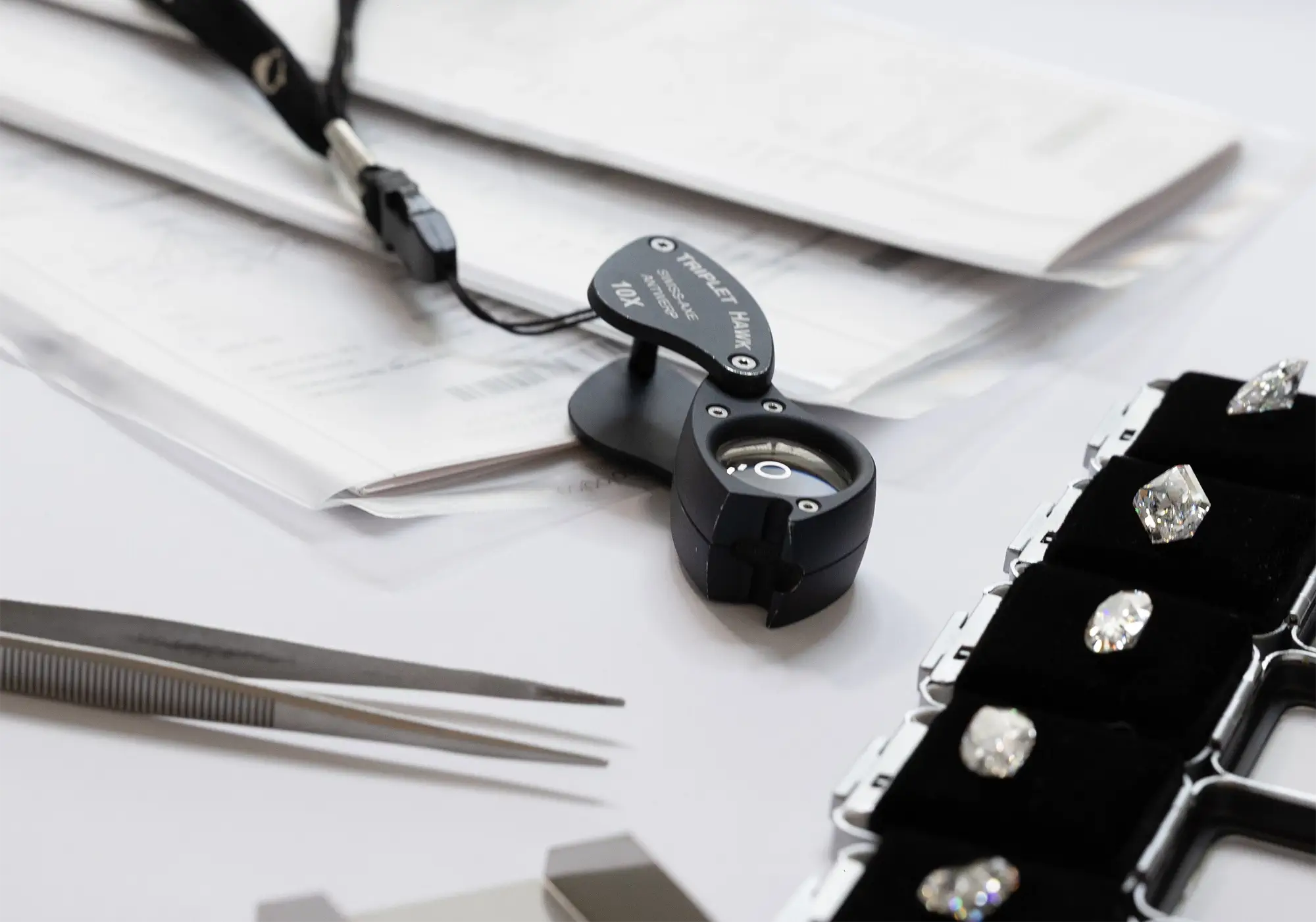Diamond inspection tools, loose diamonds and certificates displayed on a jeweler’s workbench
