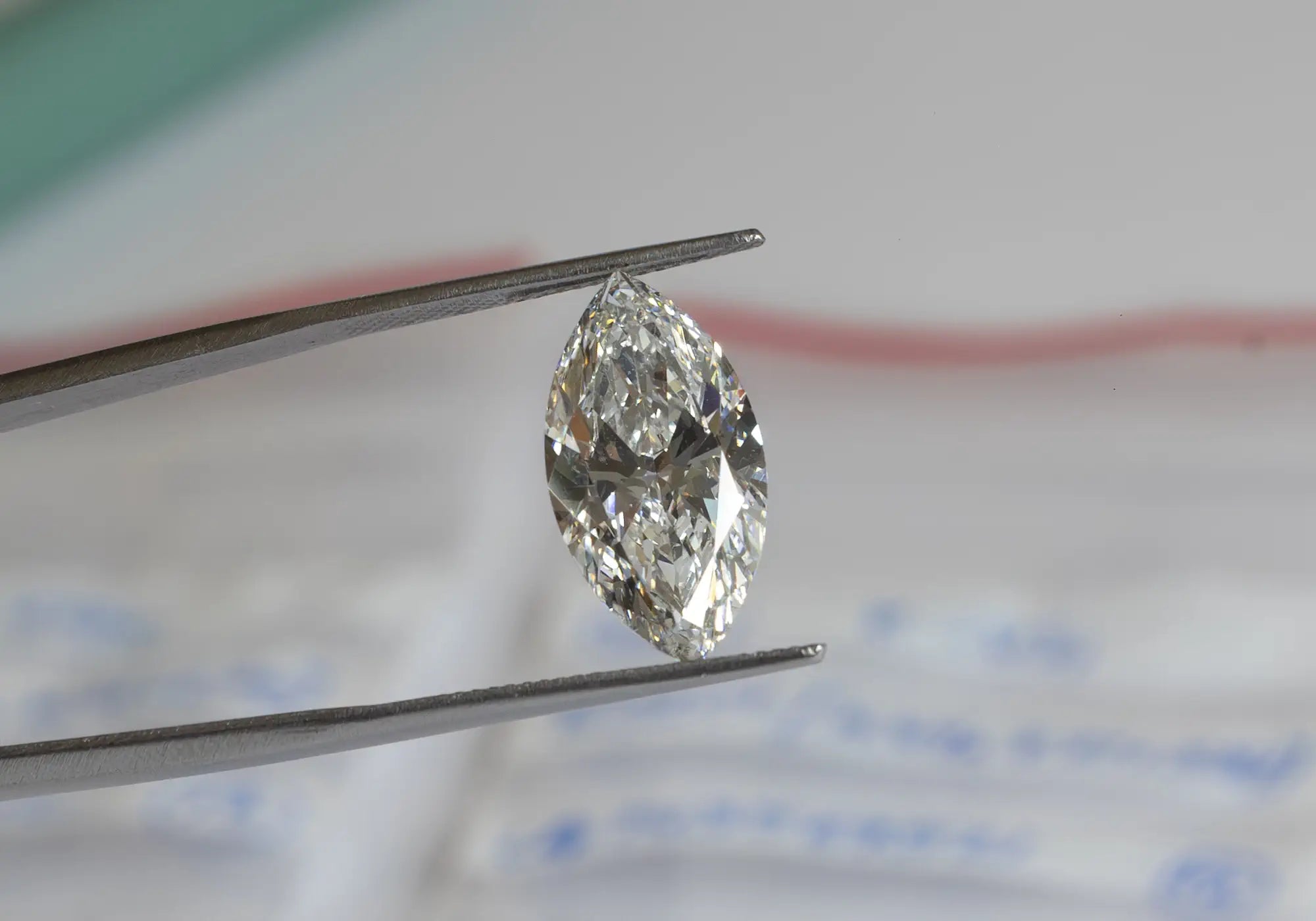 A marquise-shaped diamond is carefully held with tweezers against a soft, blurred lab background. 