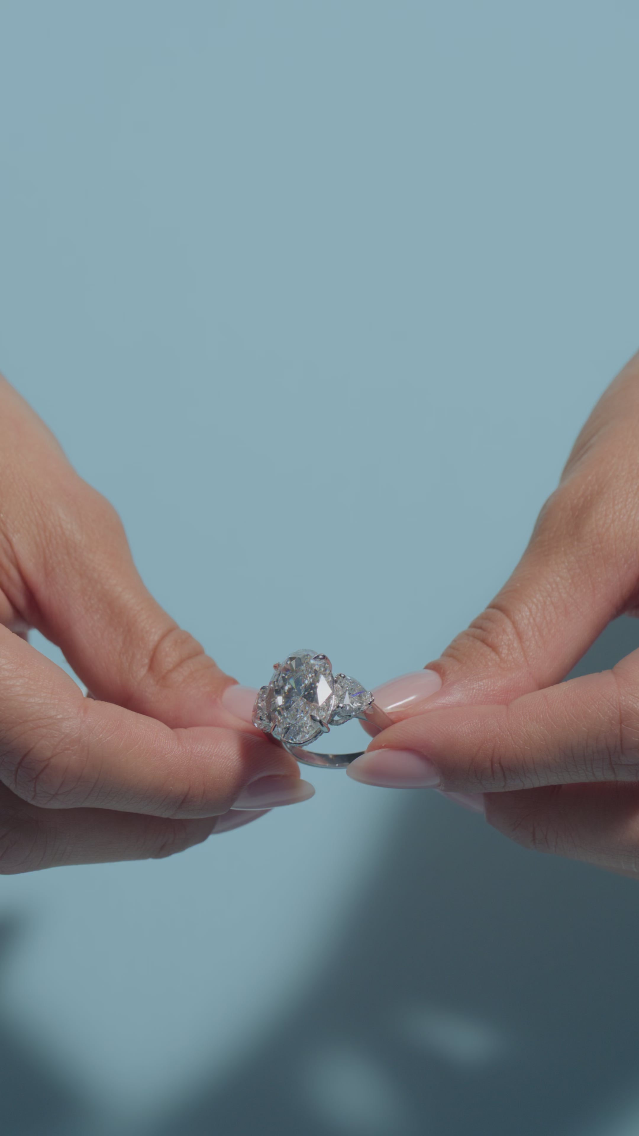 A video of an 8.09ct Oval Lab Diamond Heart Trilogy Ring  shown off by the model on a light blue background 
