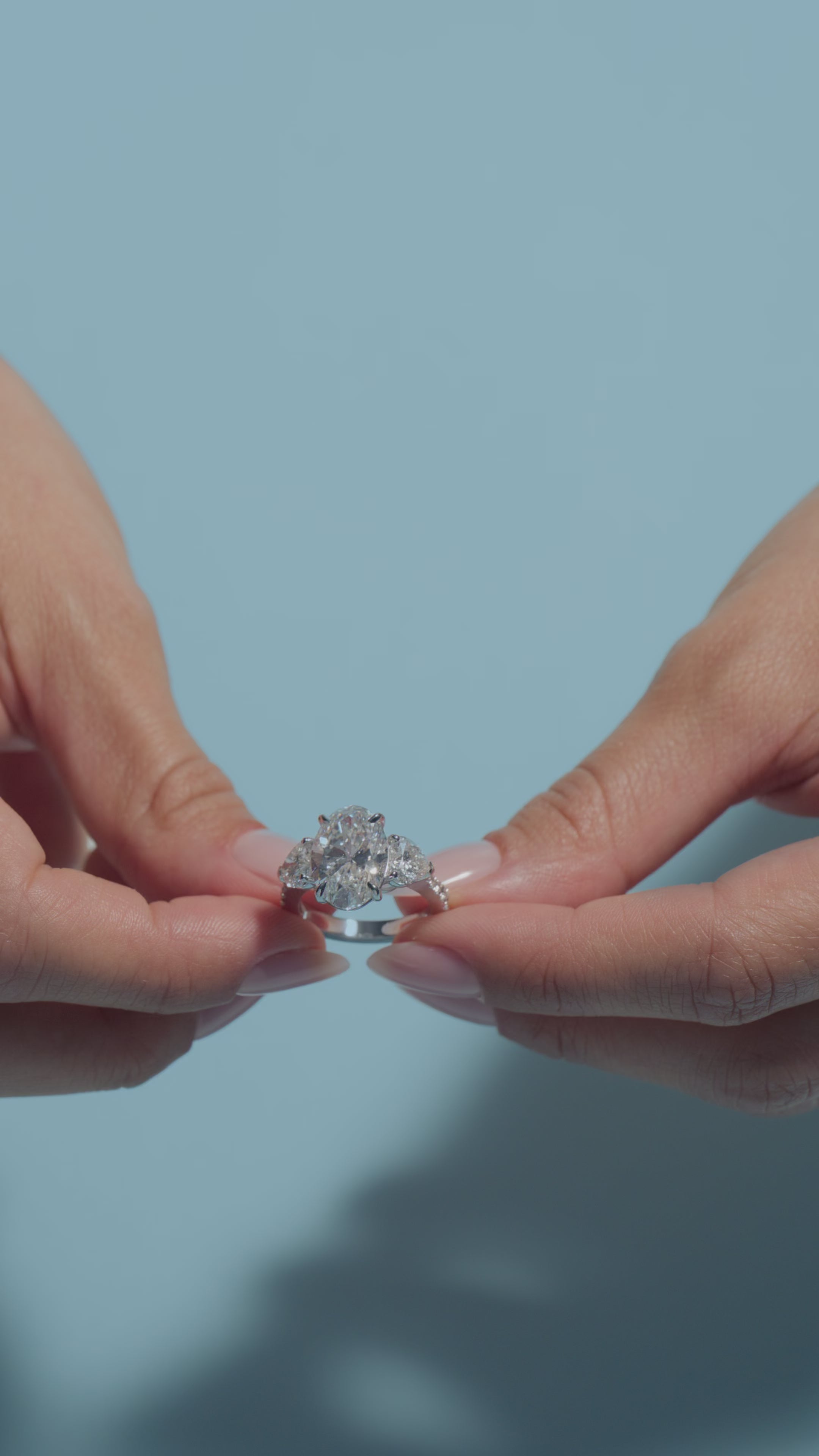Video clip of a 5.35ct Oval Lab Diamond Heart Trilogy with Reverse Shank Ring shown off by the model of BAL Diamonds on a light blue background 