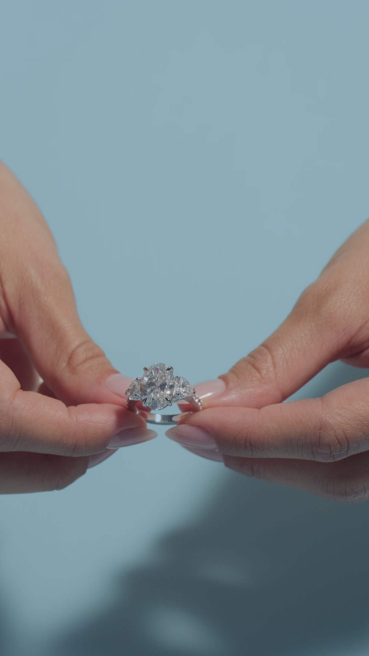 Video clip of a 5.35ct Oval Lab Diamond Heart Trilogy with Reverse Shank Ring shown off by the model of BAL Diamonds on a light blue background 