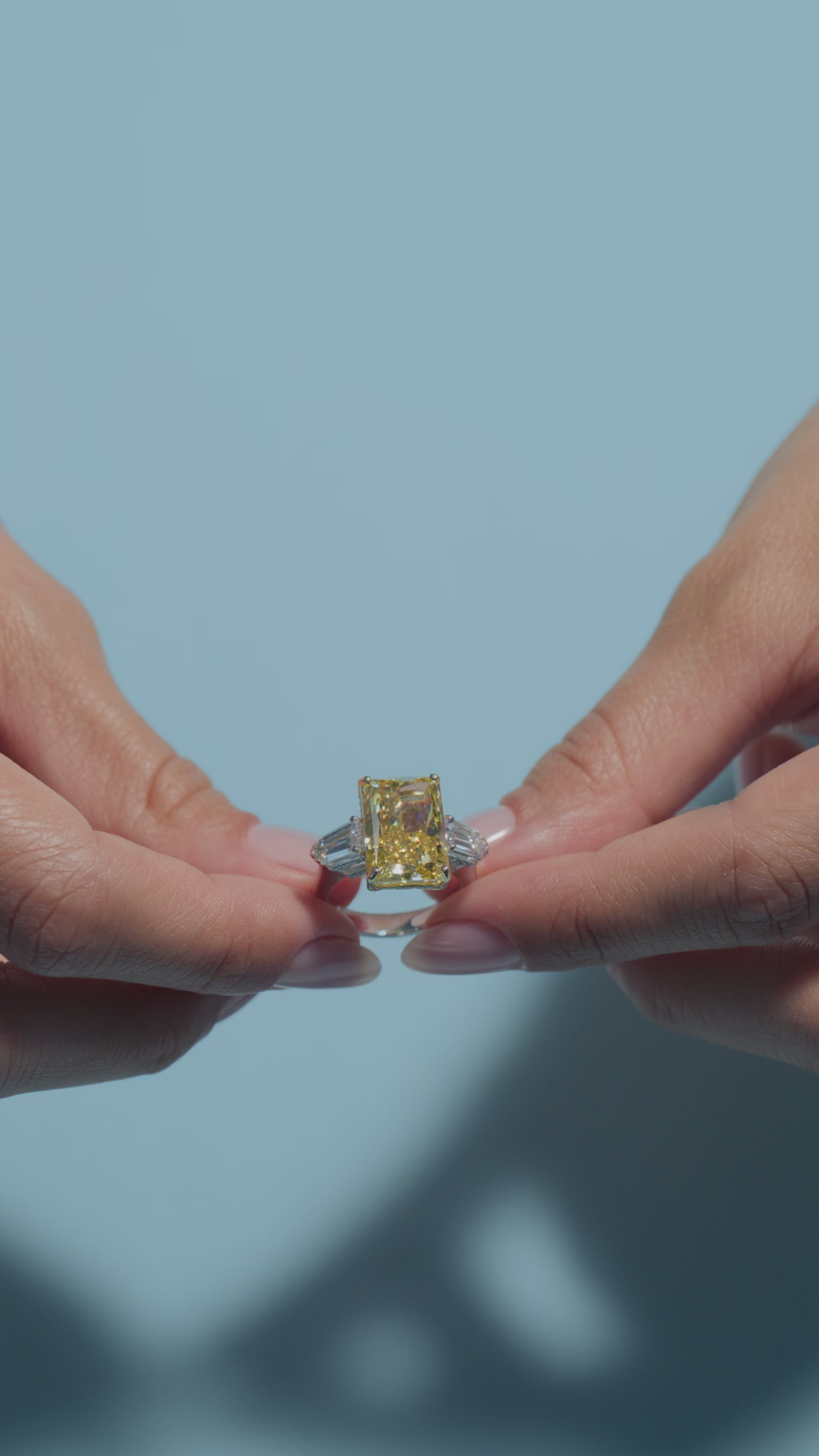 A short video presenting a 10.03ct Fancy Vivid Yellow Radiant Lab Diamond Intricate Trilogy held and worn by the model of BAL Diamonds on a light blue background