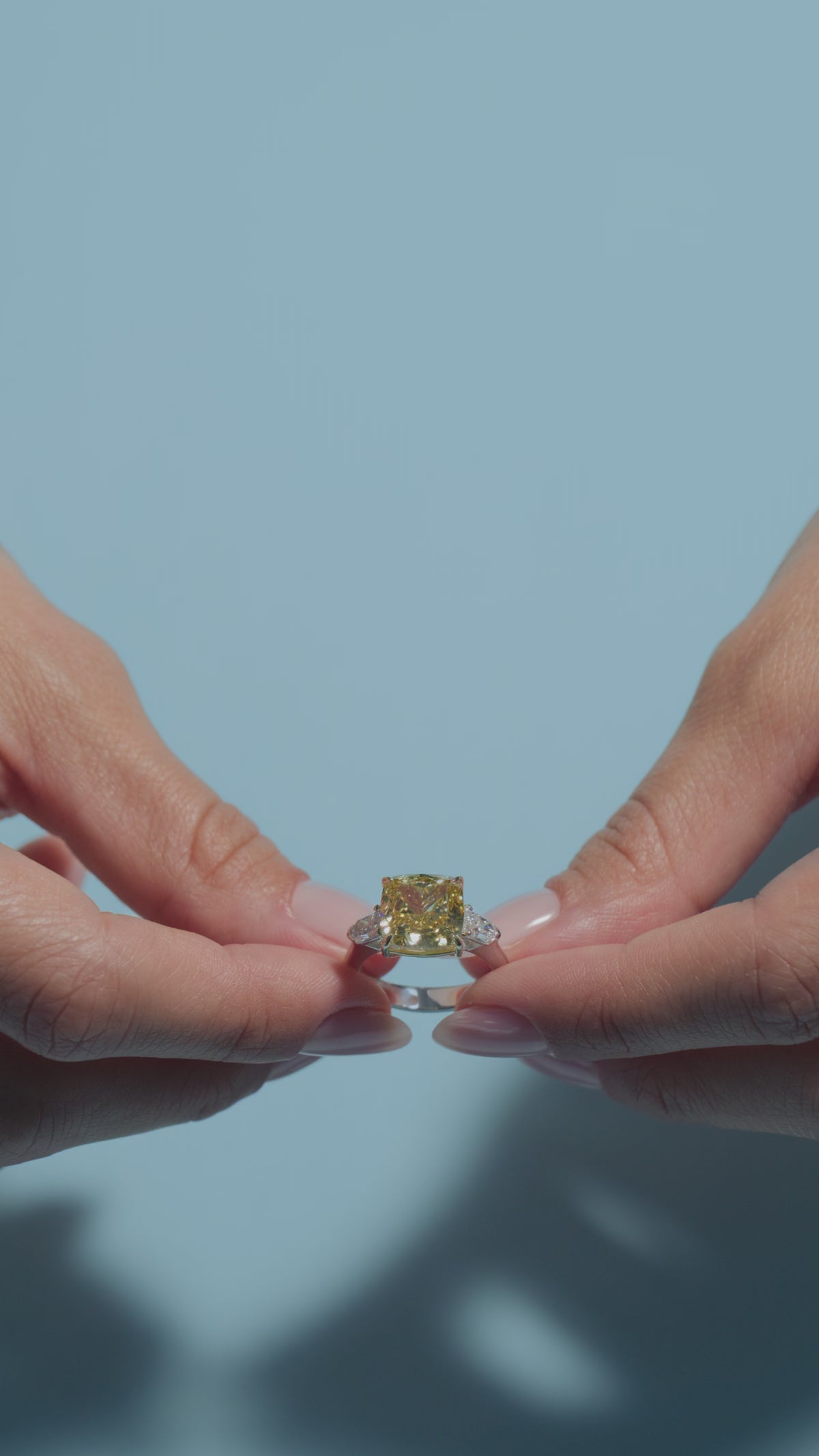 A short video of a 6.2ct Fancy Vivid Square Cushion Lab Diamond Classic Trilogy held and worn by the model of BAL Diamonds on a light blue background 