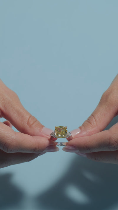 A short video of a 6.2ct Fancy Vivid Square Cushion Lab Diamond Classic Trilogy held and worn by the model of BAL Diamonds on a light blue background 