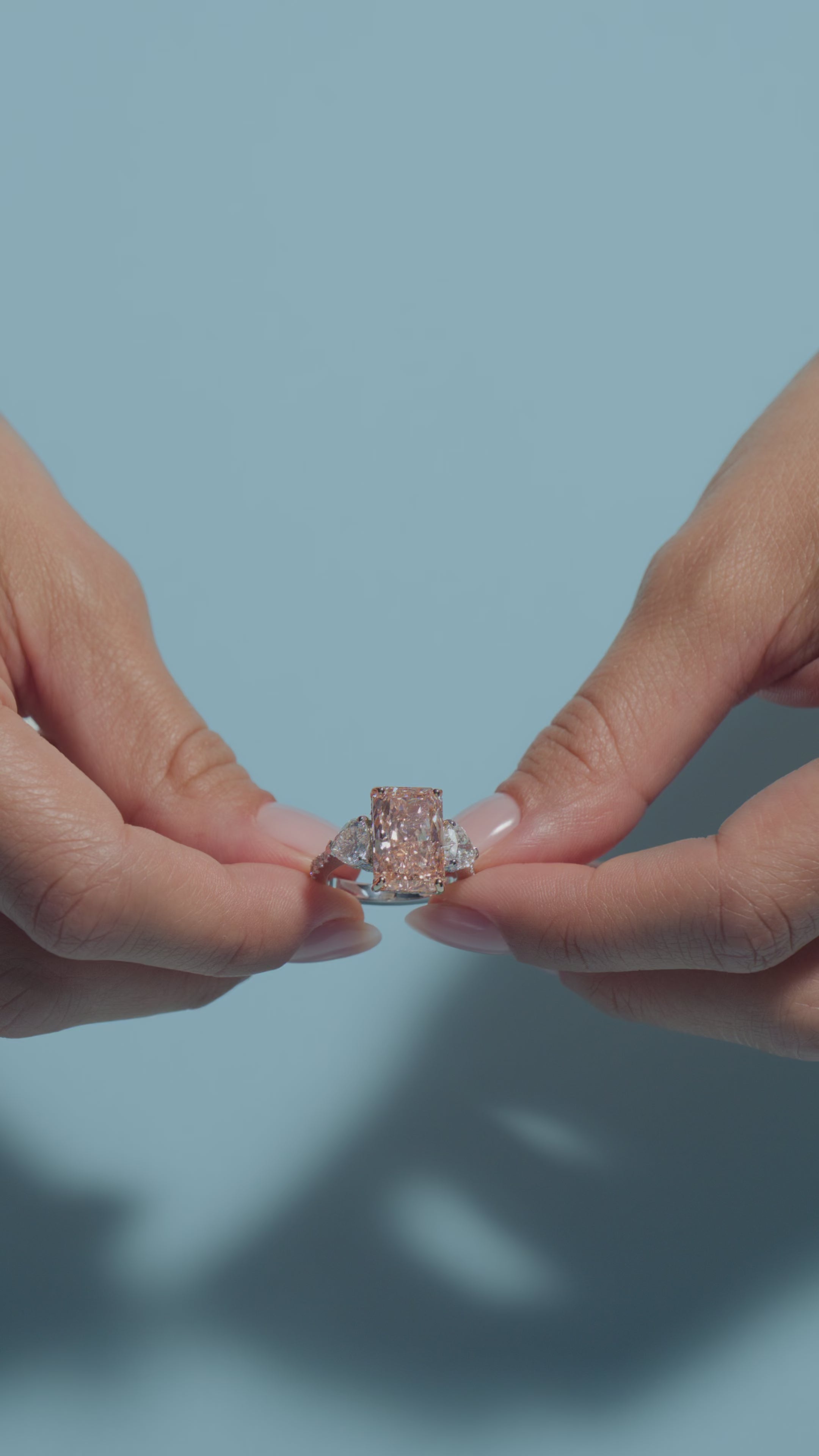 A video clip  of a 6.08ct Radiant Fancy Vivid Pink Lab Diamond Heart Trilogy Ring shown off by the model of BAL Diamonds on a light blue background