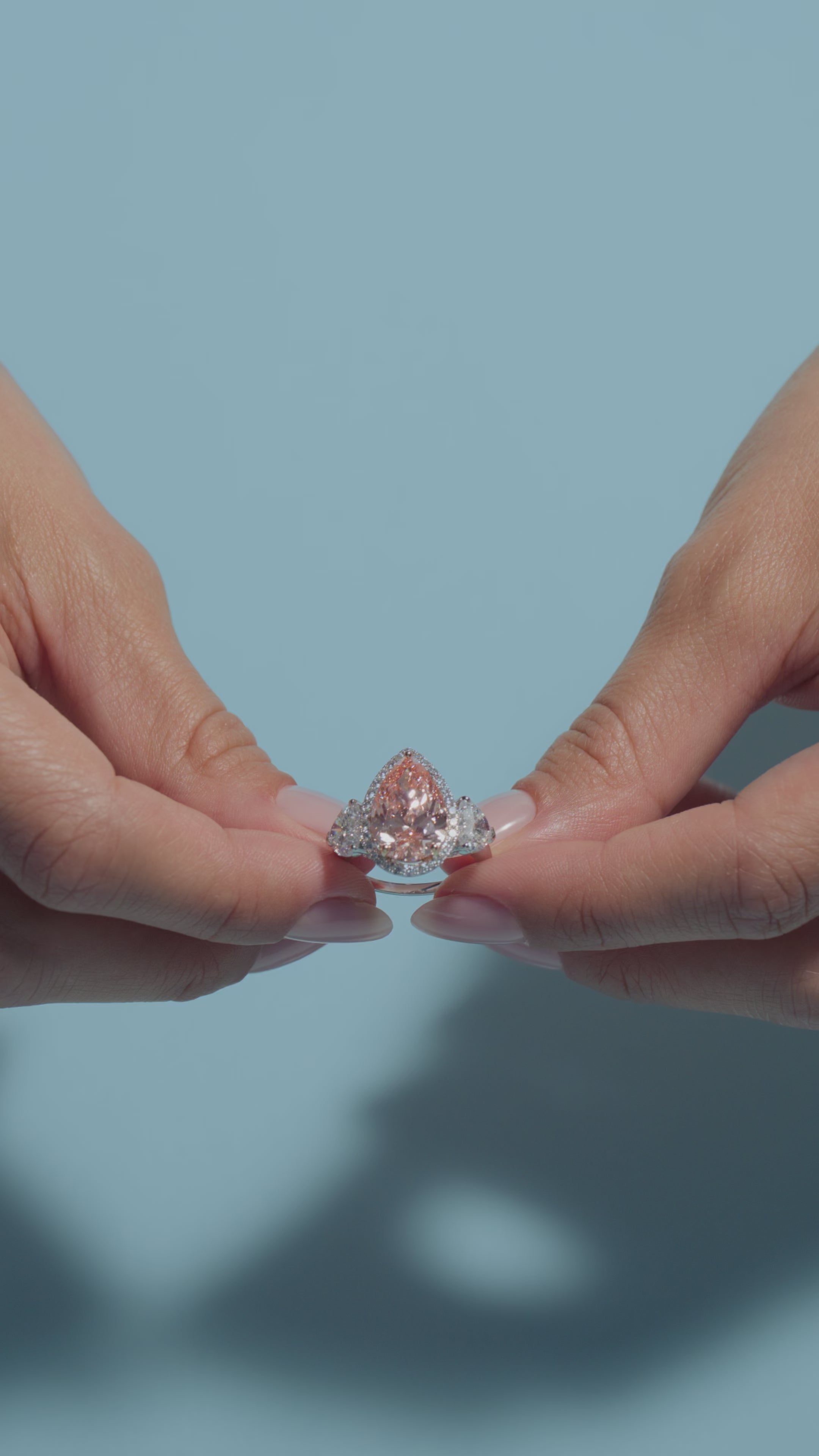 Videoclip of a 5.02ct Pear Fancy Vivid Pink Lab Diamond Heart Trilogy Ring shown off by the model on a light blue background