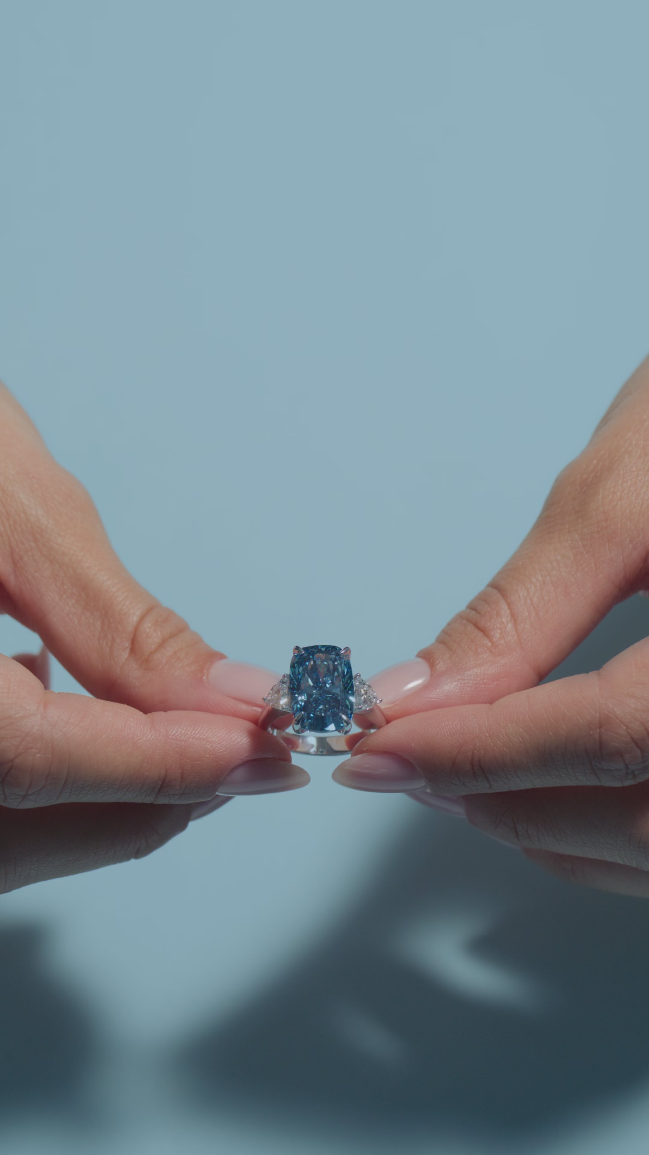 A short video featuring a 7.04ct Fancy Vivid Blue Cushion Lab Diamond Classic Trilogy Ring presented by the model of BAL Diamonds on a light blue background