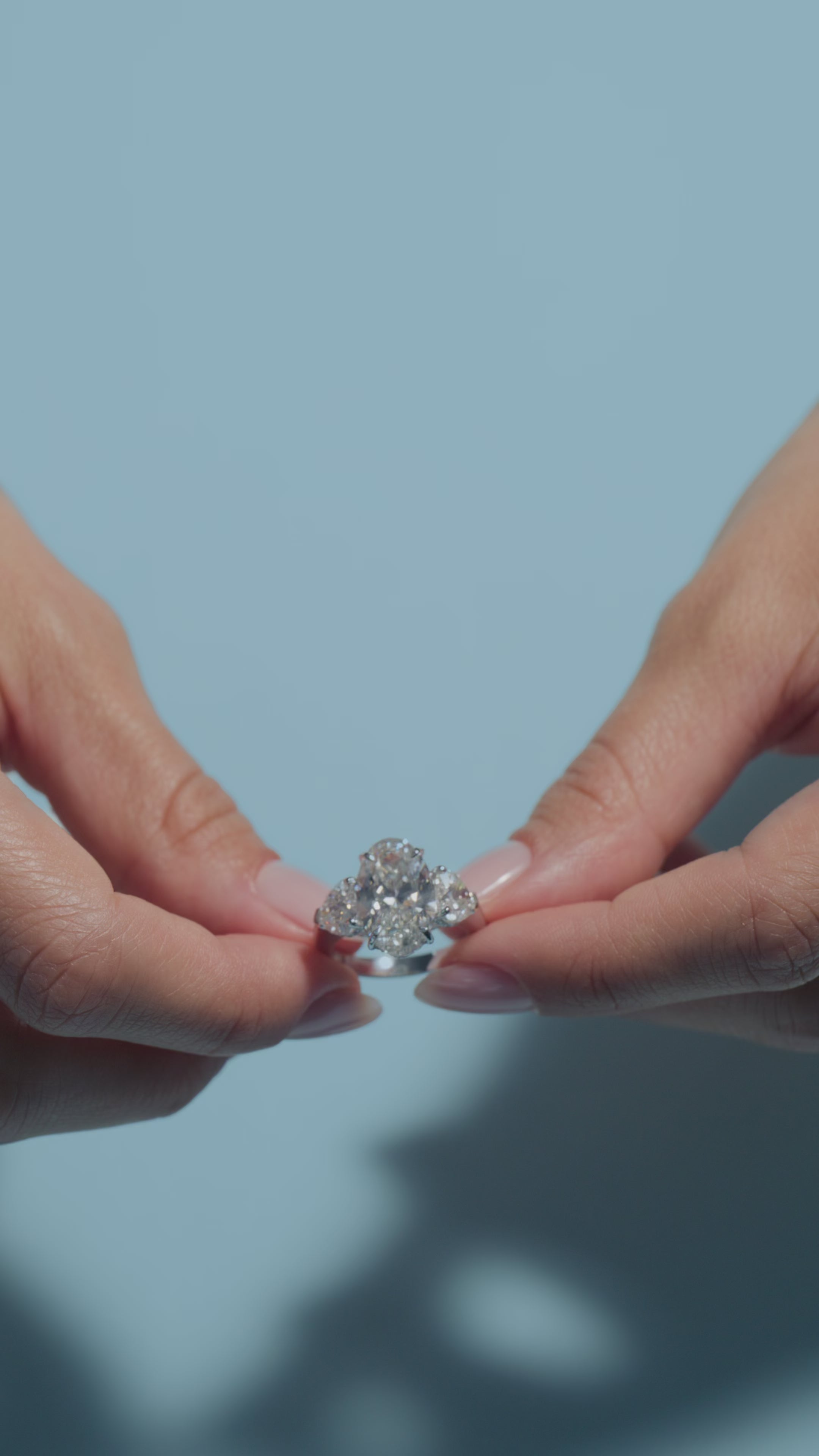 A video clip of a 5.04ct Oval Lab Diamond Heart Trilogy Ring shown off by the model in light blue background