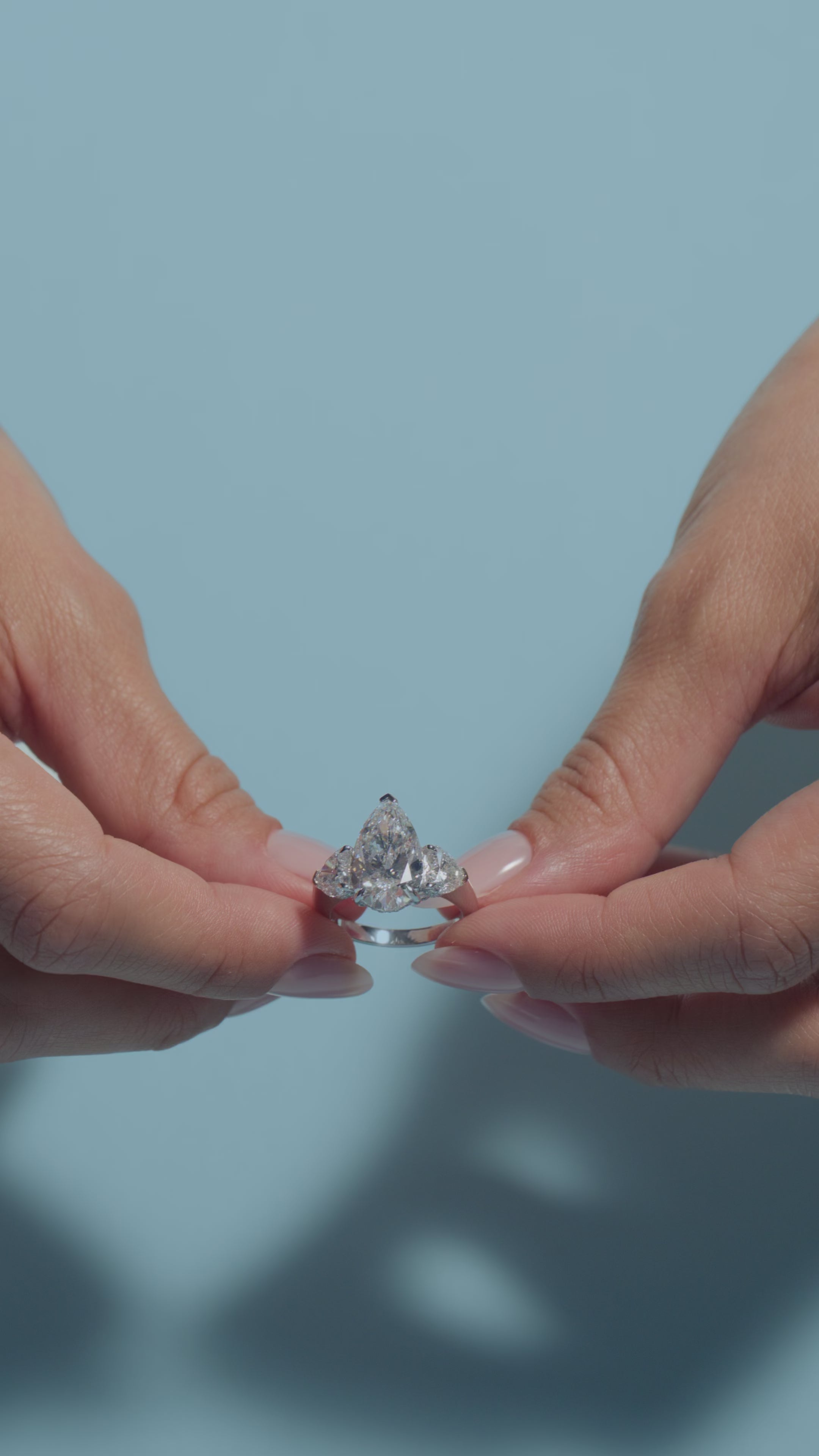 Video clip of a 5.04ct Pear Lab Diamond Heart Trilogy Ring presented by the model of BAL Diamonds on a light blue background