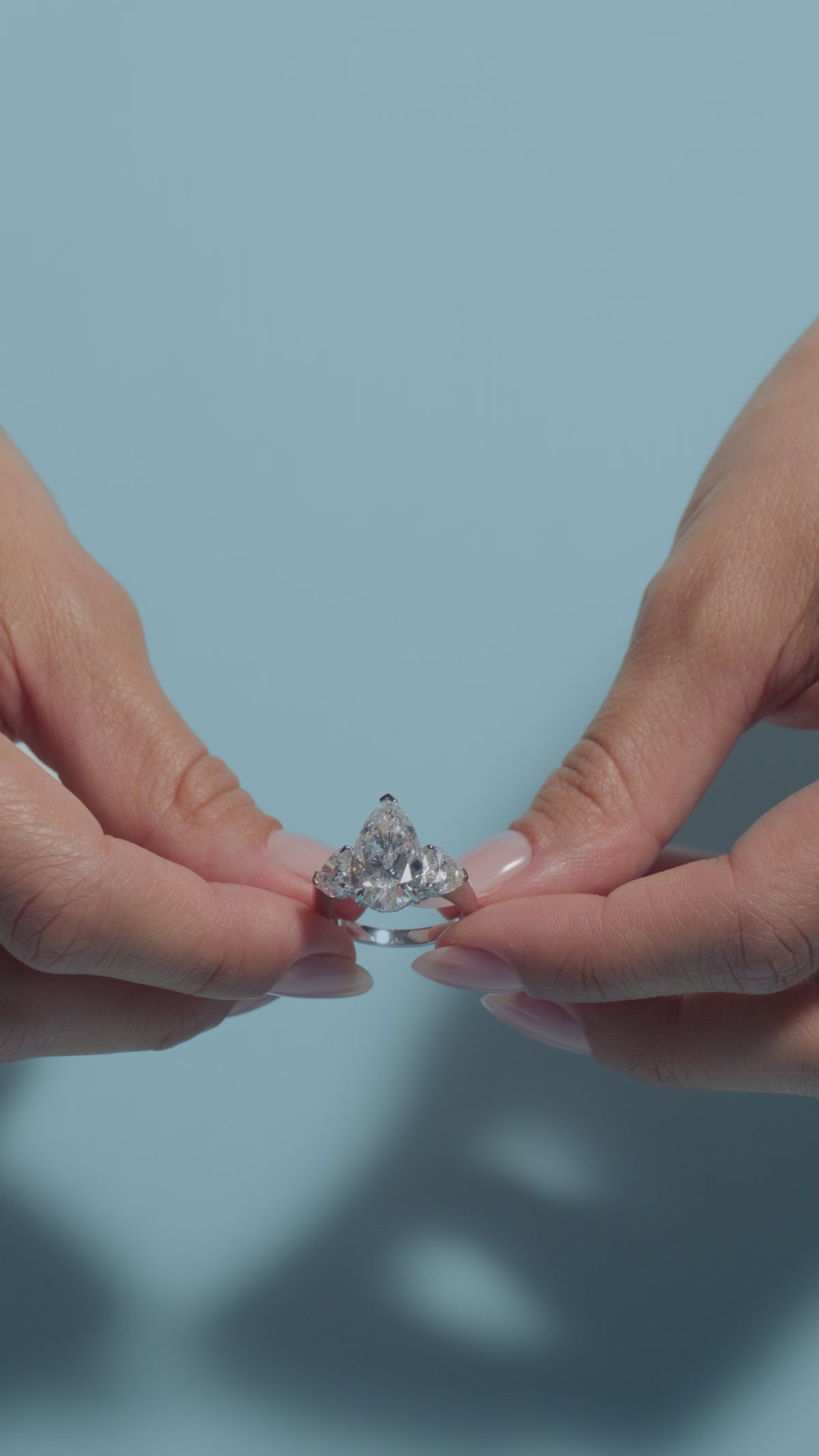 Video clip of a 5.04ct Pear Lab Diamond Heart Trilogy Ring presented by the model of BAL Diamonds on a light blue background