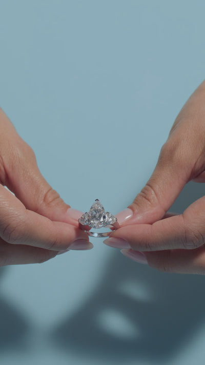 Video clip of a 5.04ct Pear Lab Diamond Heart Trilogy Ring presented by the model of BAL Diamonds on a light blue background
