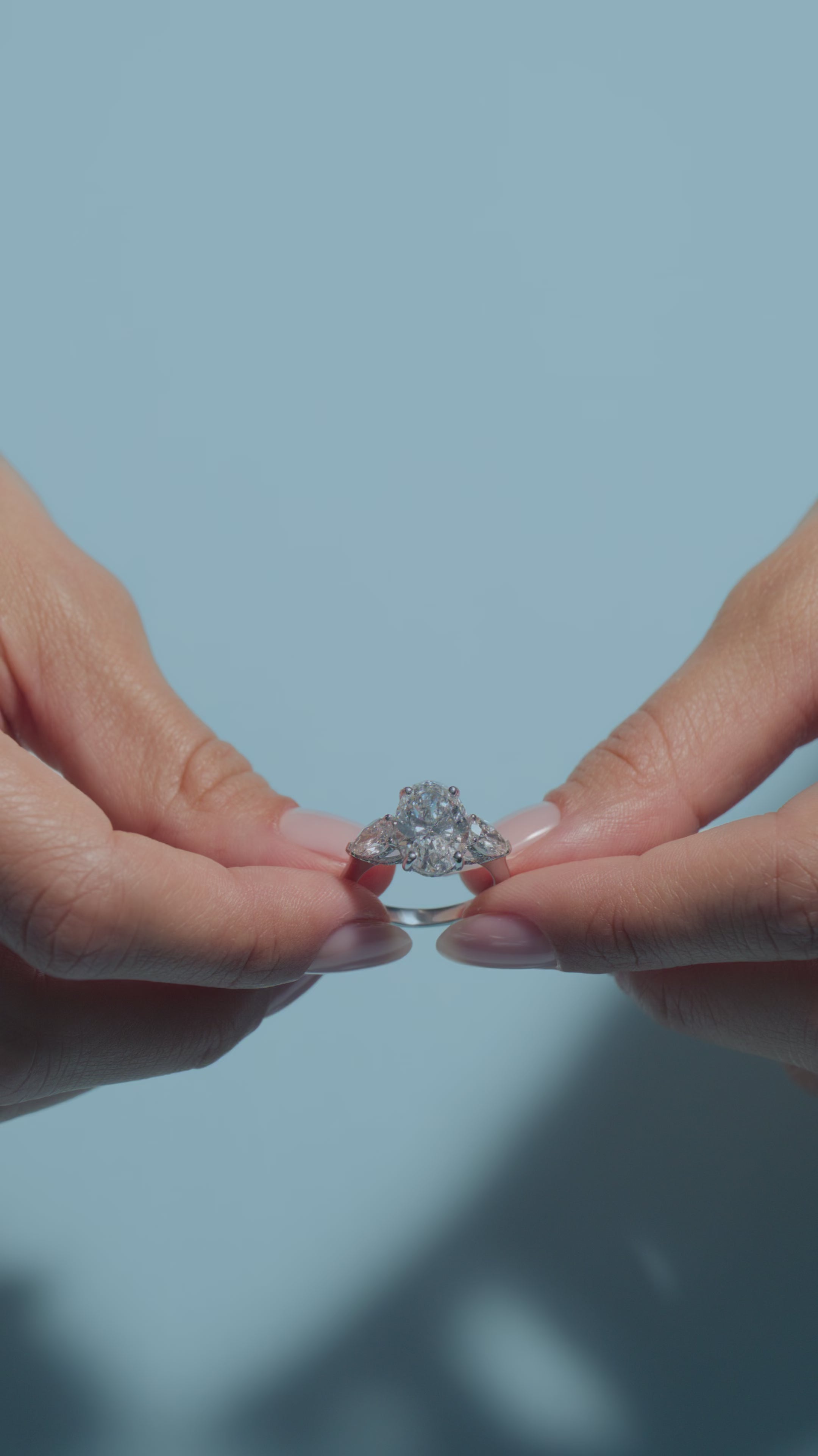 A video presentation of a 4.02ct Oval Lab Diamond Pear Trilogy Ring held and worn by the model of BAL Diamonds on a light blue background