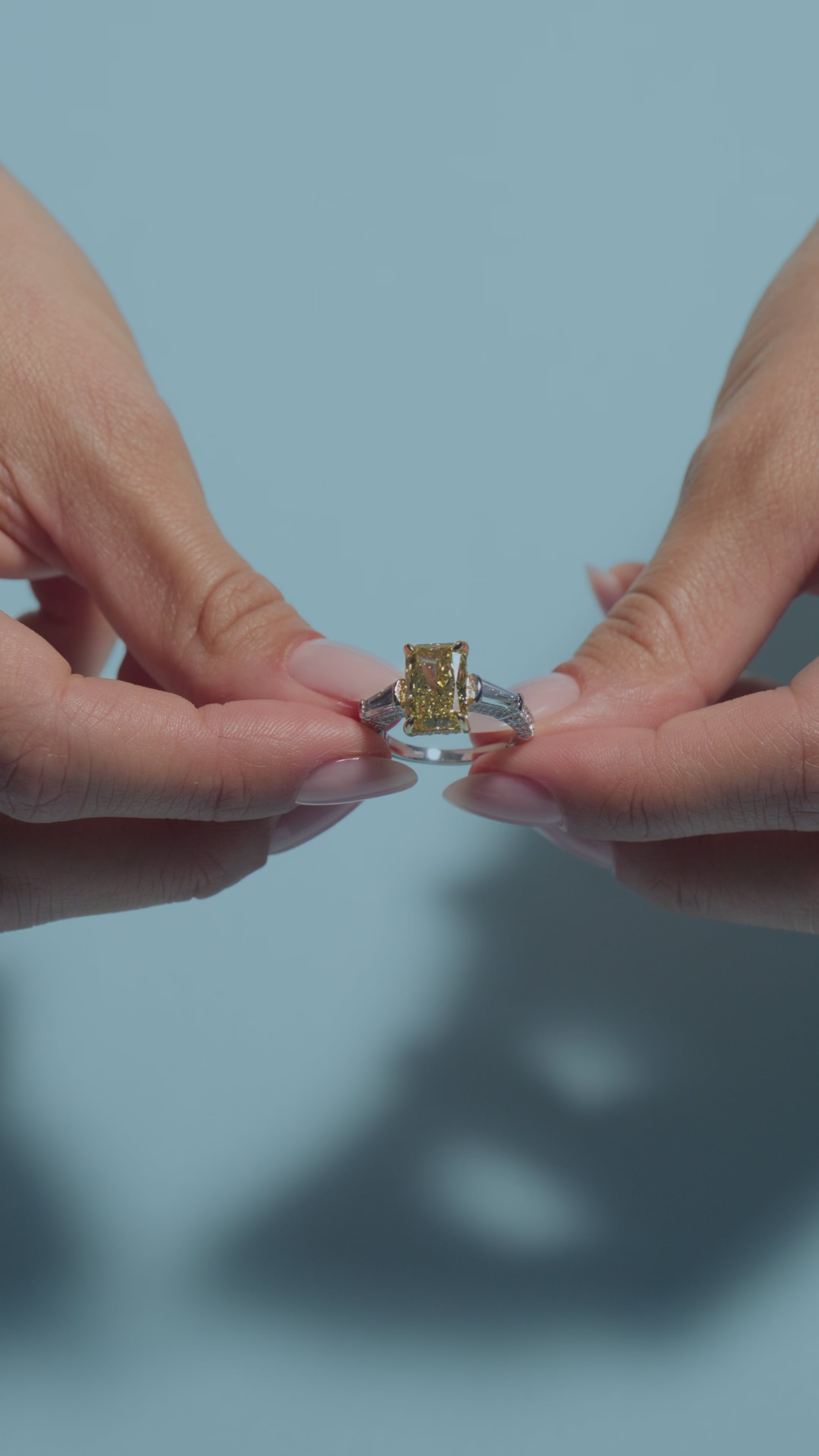 A video of a 3.52ct Radiant Fancy Vivid Yellow Lab Diamond Tapers Trilogy Ring   presented by the model of BAL Diamonds on a light blue background 