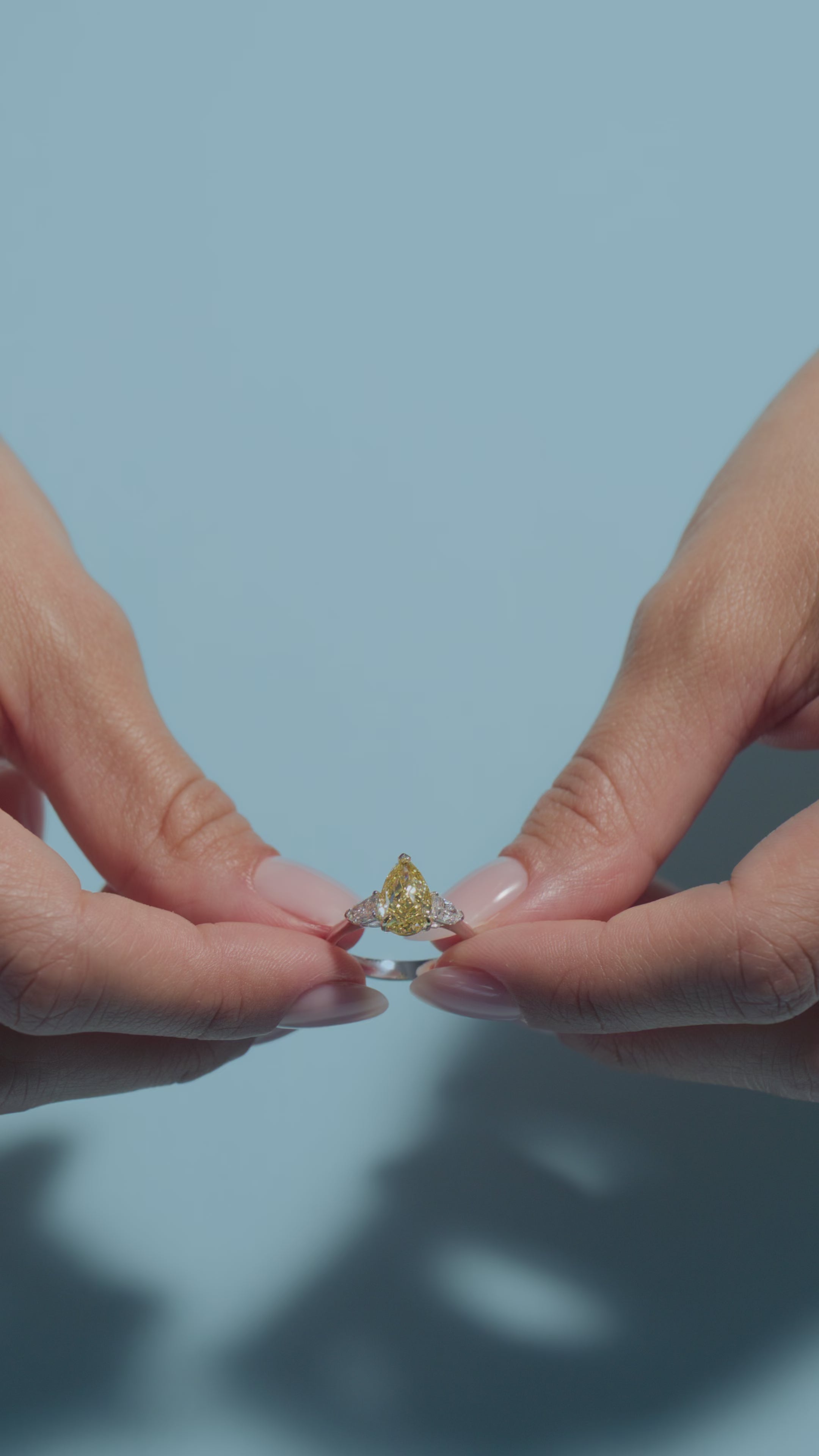 A video featuring a 2.07ct Fancy Intense Yellow Pear Lab Diamond Classic Trilogy Ring held and worn by the model of BAL Diamonds on a light blue background
